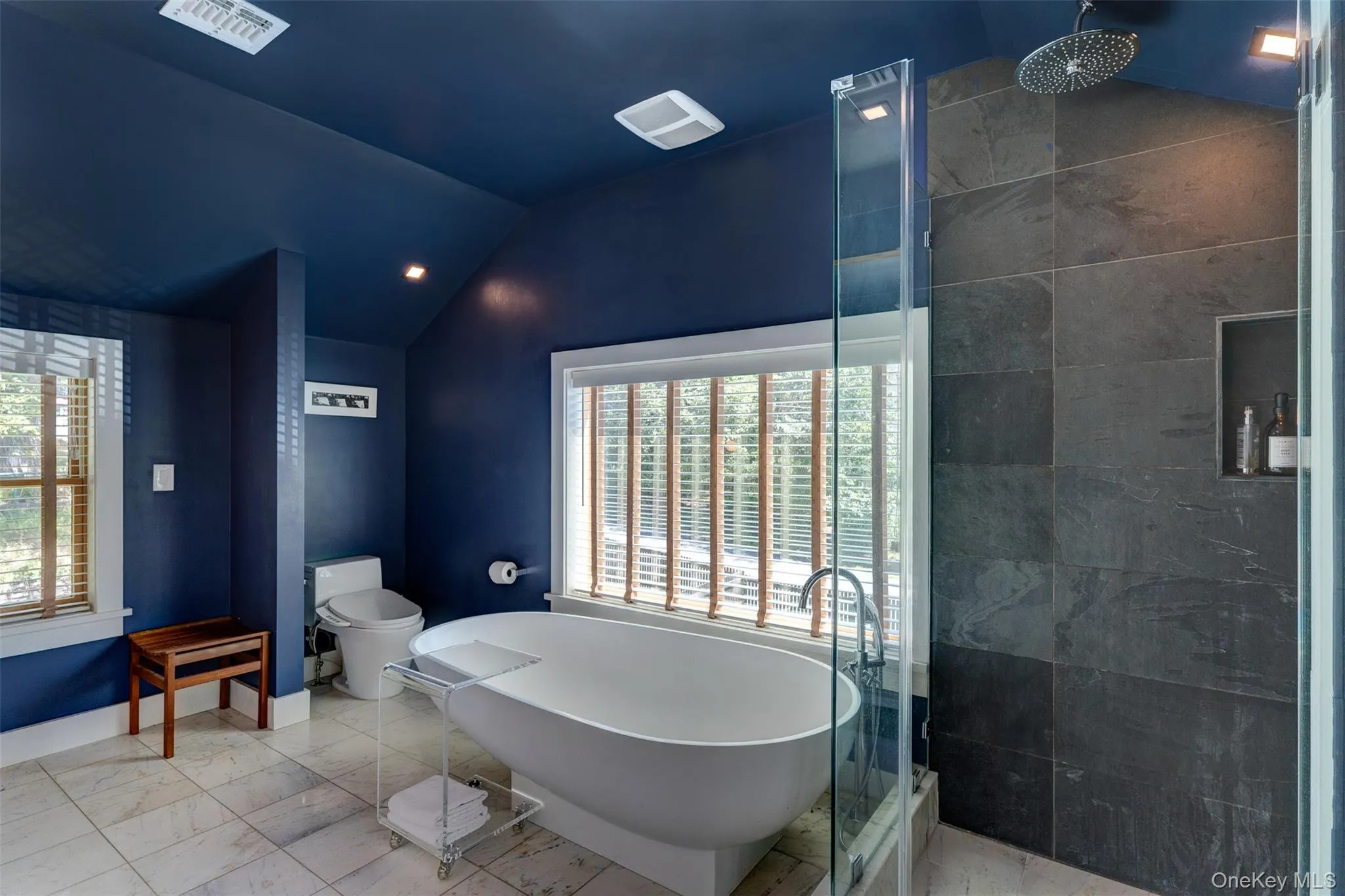 Bathroom featuring vaulted ceiling, a freestanding tub, marble look tile flooring, and a tile shower Bathroom featuring vaulted ceiling, a freestanding tub, marble look tile flooring, and a tile shower