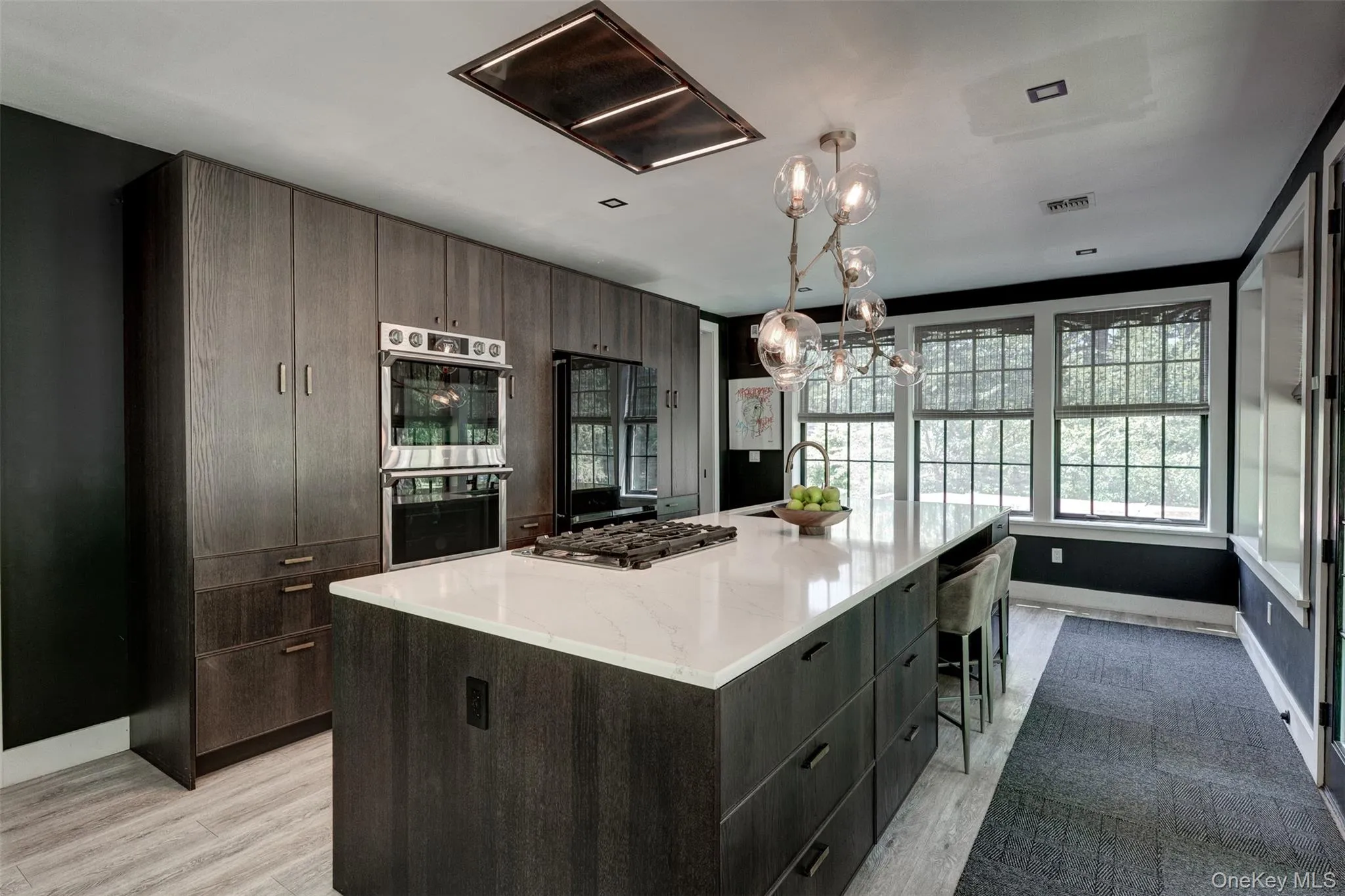Kitchen with modern cabinets, stainless steel appliances, hanging light fixtures, a chandelier, and a spacious island Kitchen with modern cabinets, stainless steel appliances, hanging light fixtures, a chandelier, and a spacious island