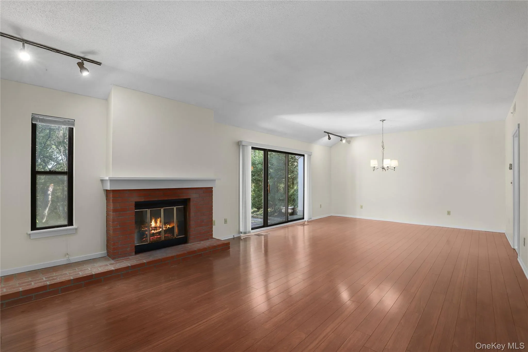 Living room /Dining Room featuring track lighting, a brick fireplace, wood finished floors, and a chandelier Living room /Dining Room featuring track lighting, a brick fireplace, wood finished floors, and a chandelier