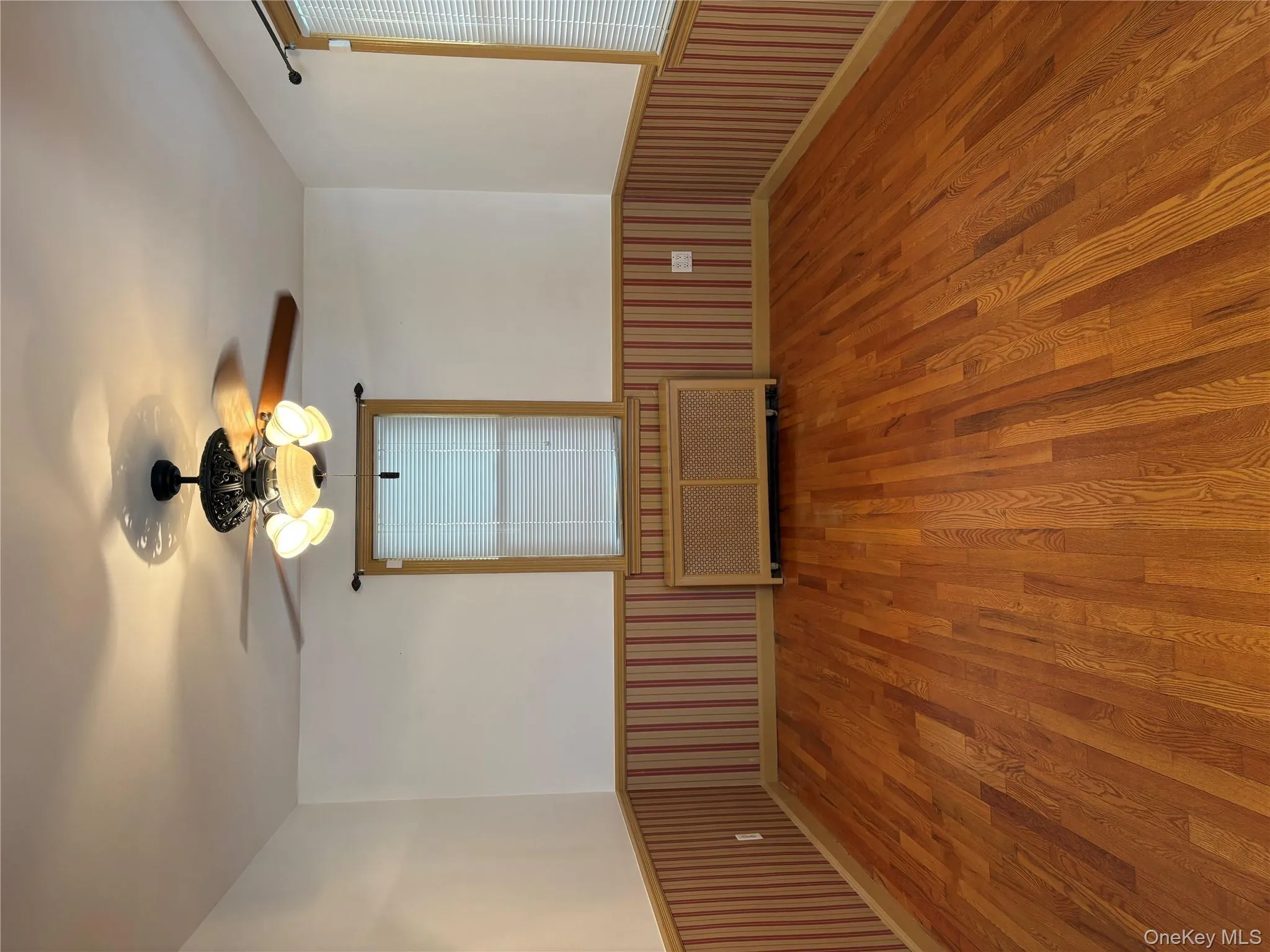 Empty room with a wainscoted wall, a ceiling fan, wood finished floors, and radiator heating unit Empty room with a wainscoted wall, a ceiling fan, wood finished floors, and radiator heating unit
