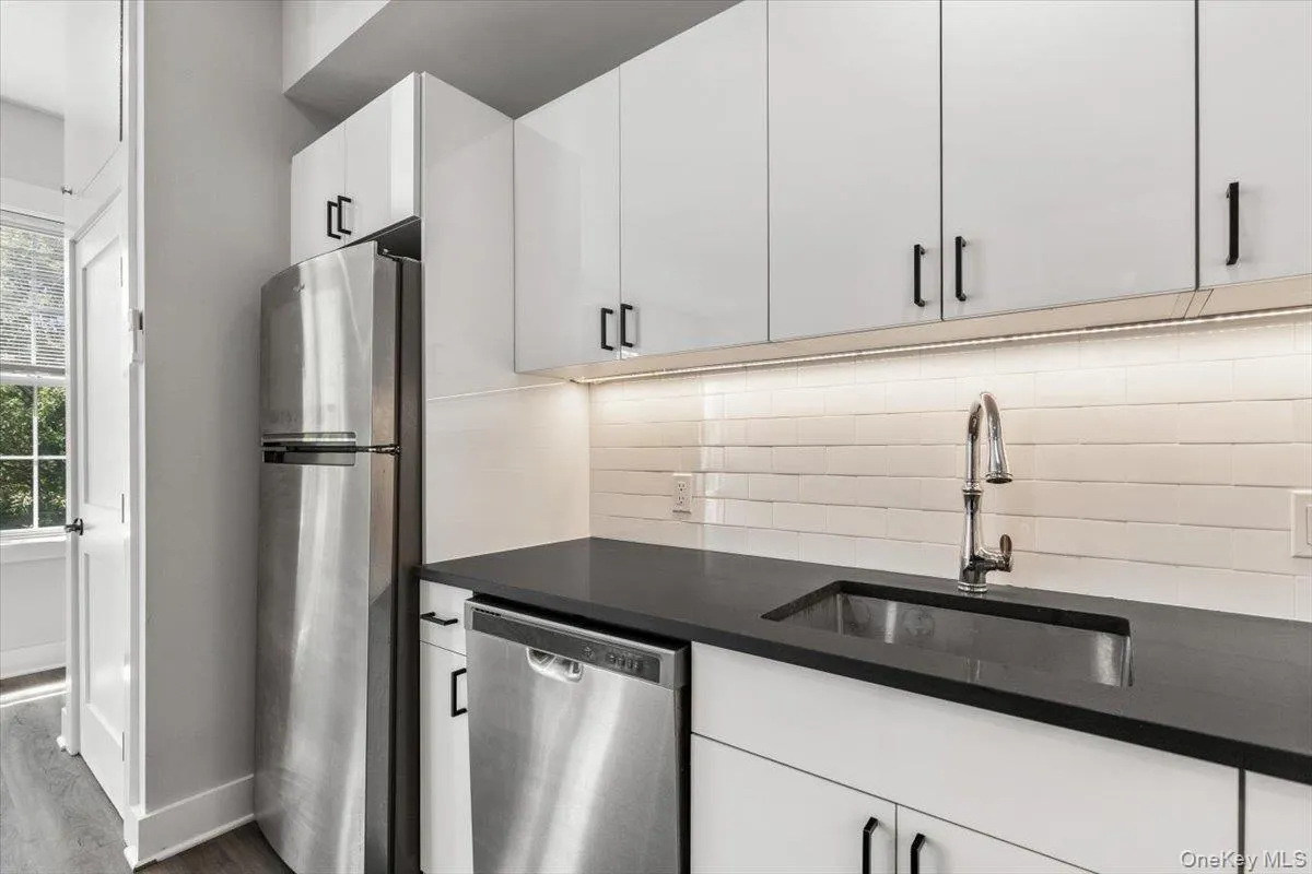 Kitchen with stainless steel appliances, white cabinets, tasteful backsplash, dark stone countertops, and dark wood-style floors Kitchen with stainless steel appliances, white cabinets, tasteful backsplash, dark stone countertops, and dark wood-style floors