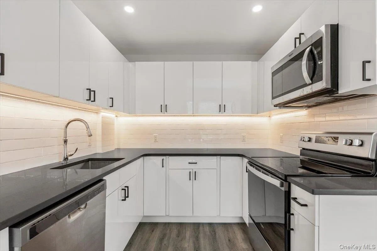 Kitchen featuring stainless steel appliances, light wood-style floors, dark stone counters, white cabinets, and recessed lighting Kitchen featuring stainless steel appliances, light wood-style floors, dark stone counters, white cabinets, and recessed lighting