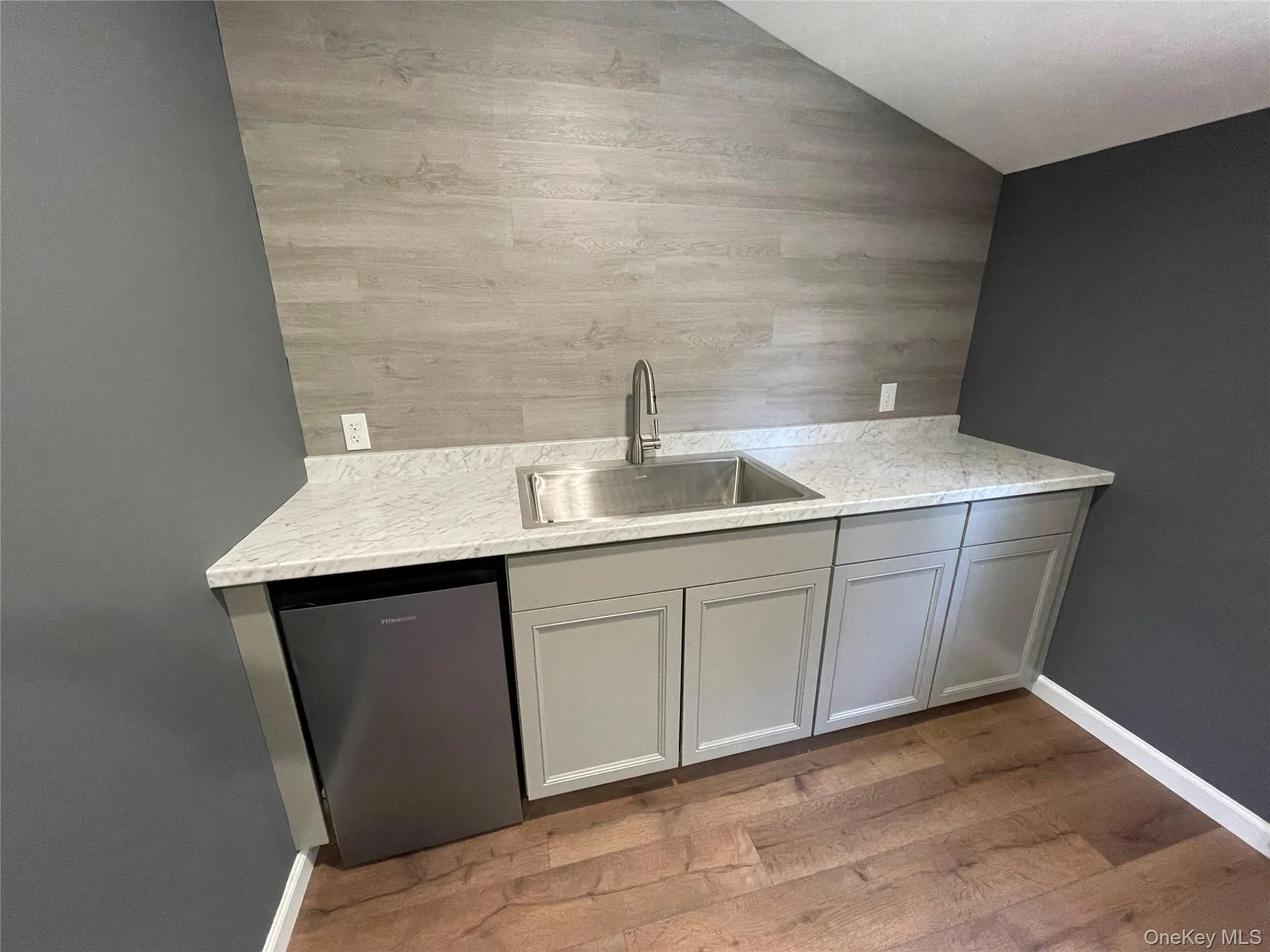 Bar featuring gray cabinets, light wood-style flooring, light stone counters, and stainless steel dishwasher Bar featuring gray cabinets, light wood-style flooring, light stone counters, and stainless steel dishwasher