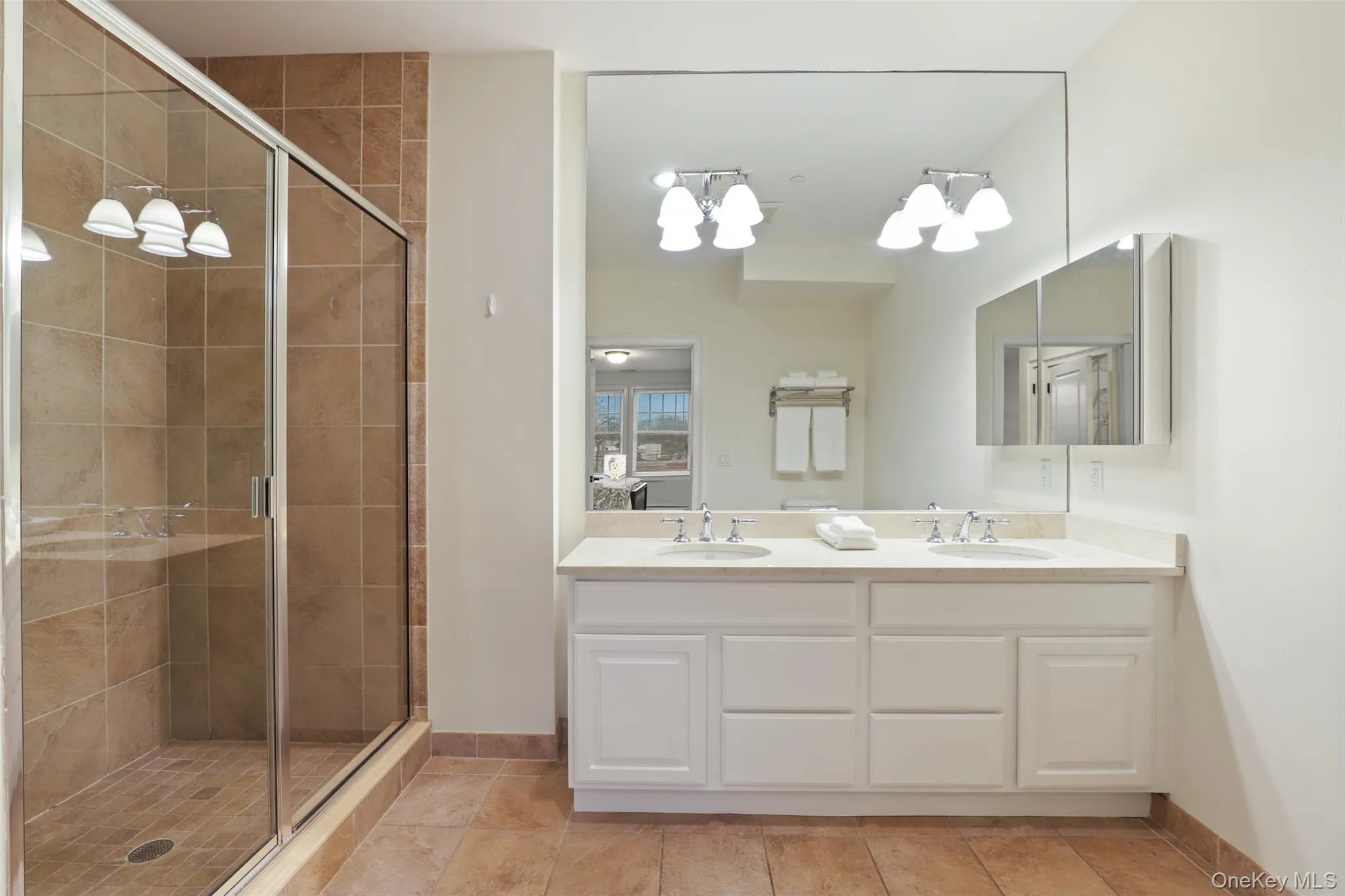 Full bathroom featuring a shower stall, double vanity, a chandelier, and light tile patterned floors Full bathroom featuring a shower stall, double vanity, a chandelier, and light tile patterned floors