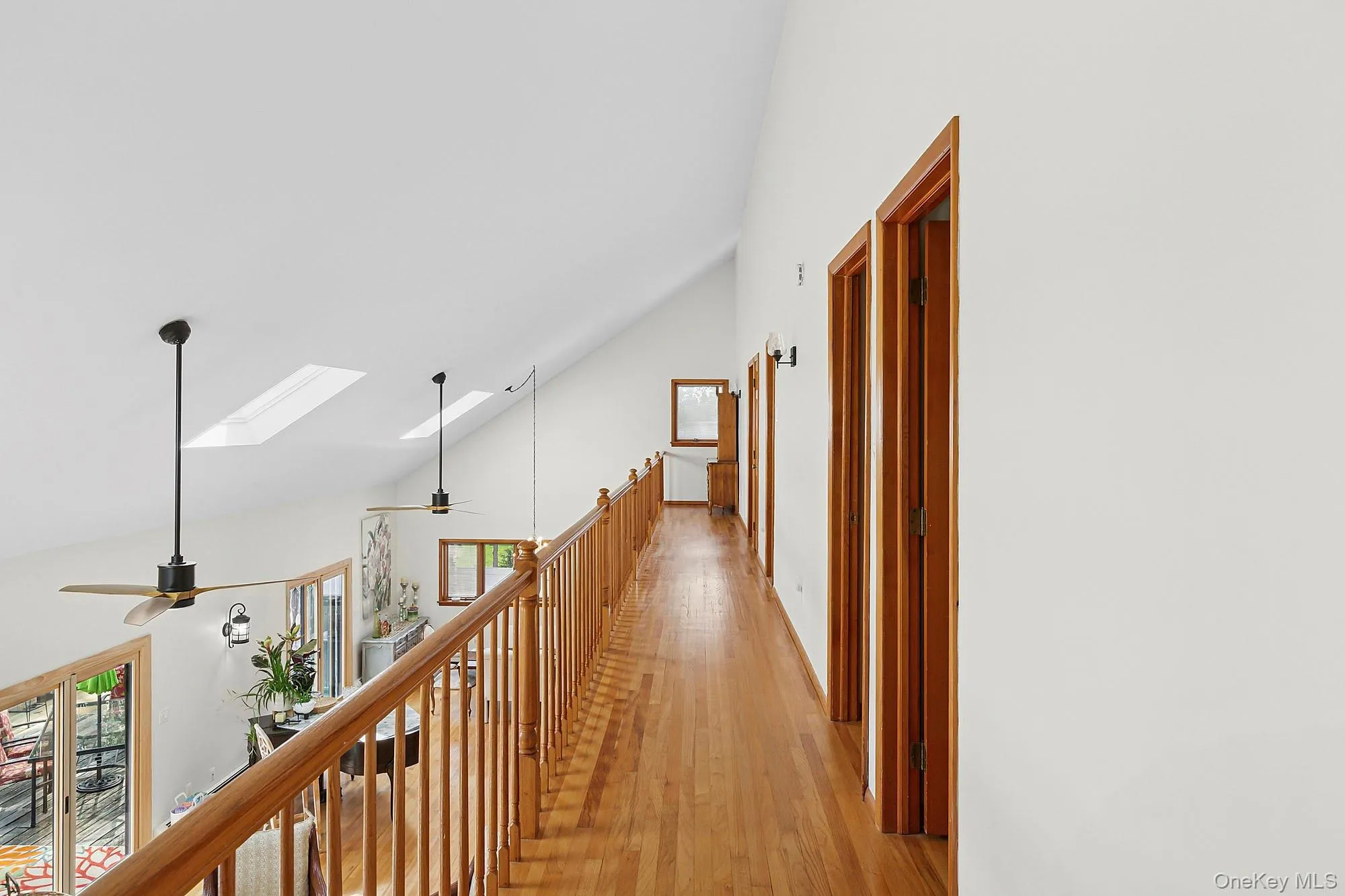 Corridor featuring high vaulted ceiling, a skylight, wood finished floors, and an upstairs landing Corridor featuring high vaulted ceiling, a skylight, wood finished floors, and an upstairs landing