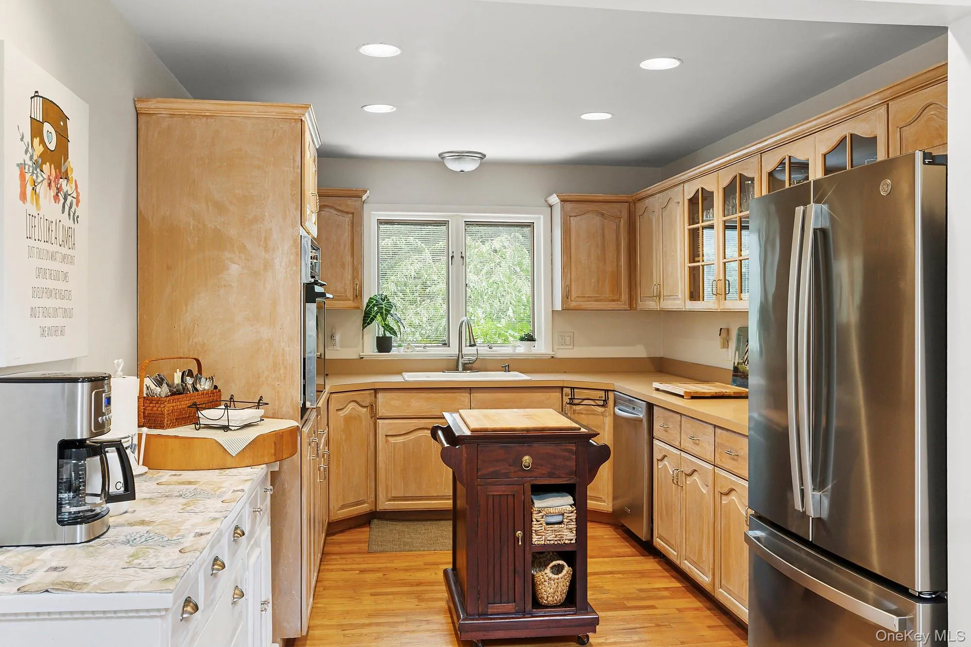 Kitchen with stainless steel appliances, glass insert cabinets, light wood-style floors, light brown cabinets, and recessed lighting Kitchen with stainless steel appliances, glass insert cabinets, light wood-style floors, light brown cabinets, and recessed lighting