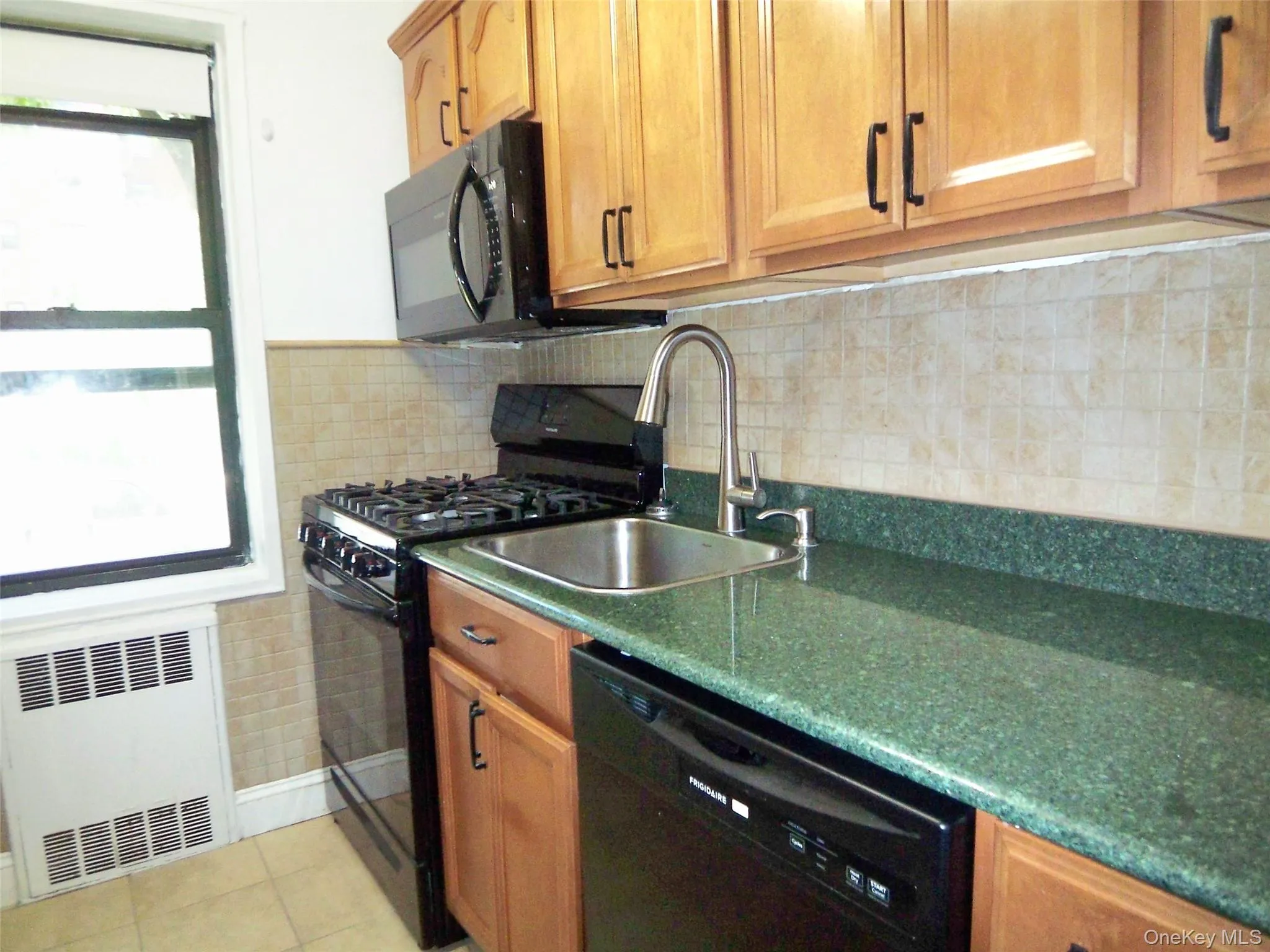 Kitchen featuring black appliances, radiator, backsplash, and plenty of natural light Kitchen featuring black appliances, radiator, backsplash, and plenty of natural light