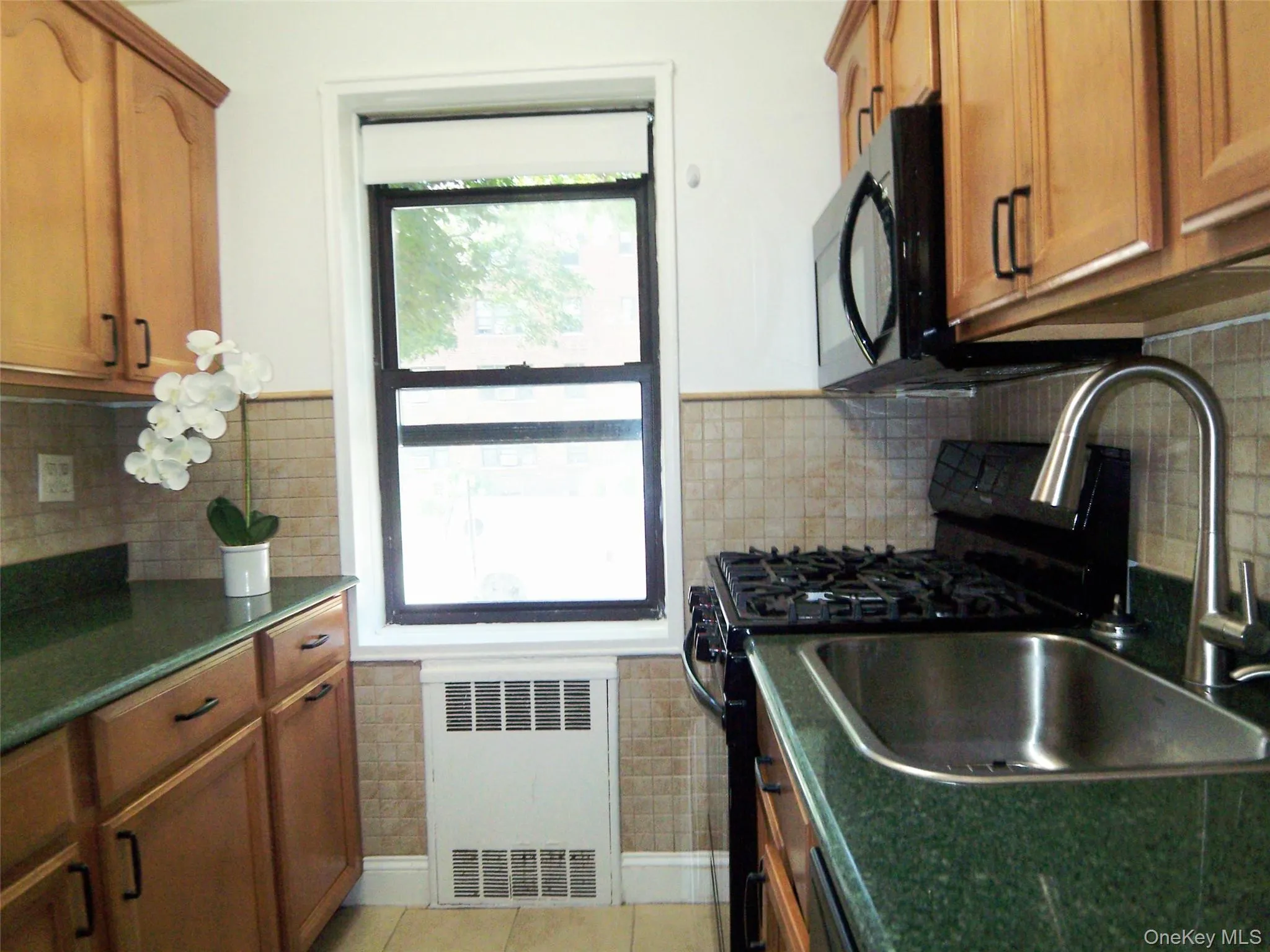 Kitchen with brown cabinets, radiator, light tile patterned flooring, and decorative backsplash Kitchen with brown cabinets, radiator, light tile patterned flooring, and decorative backsplash