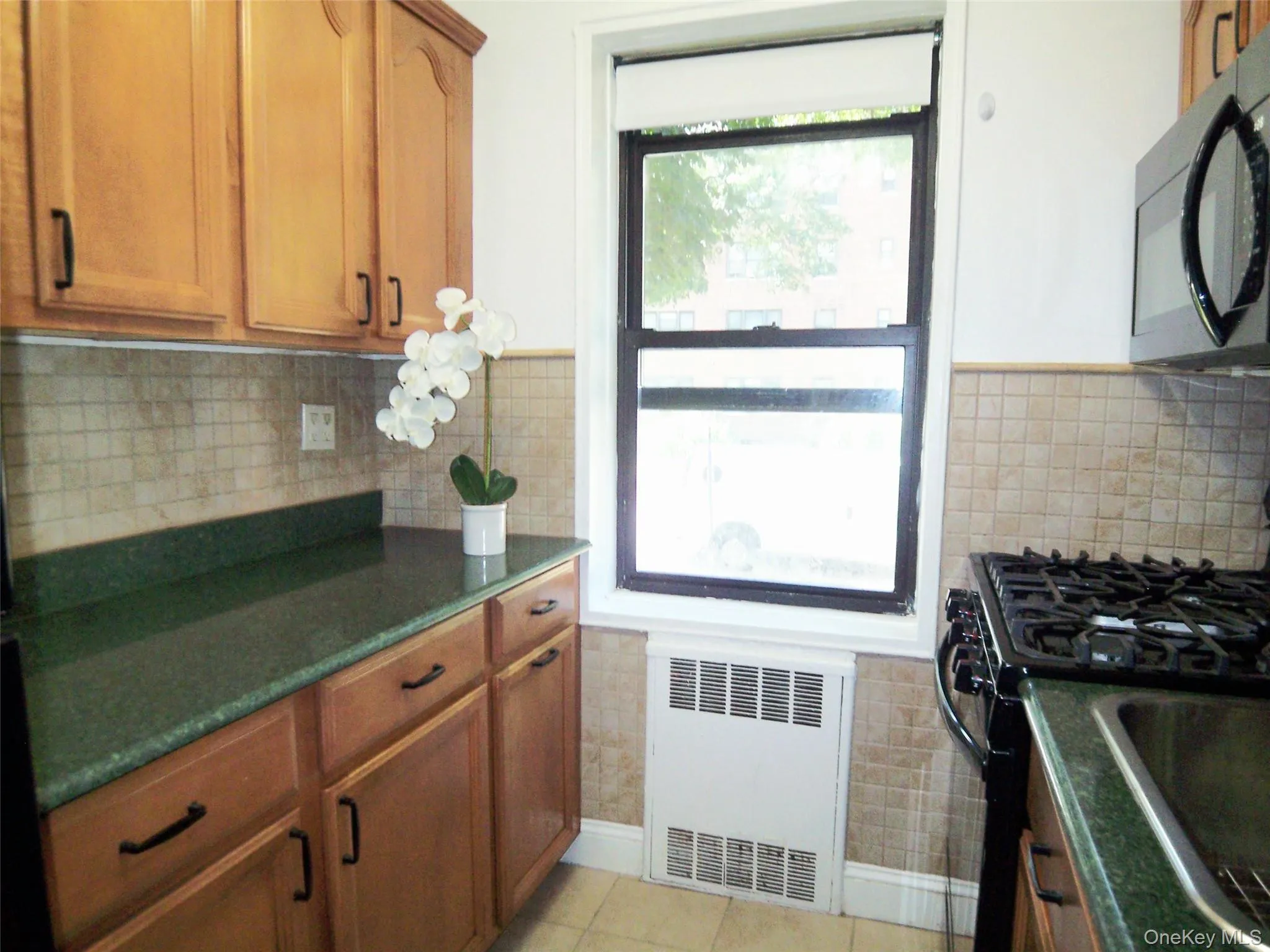 Kitchen featuring healthy amount of natural light, dark countertops, radiator heating unit, and black microwave Kitchen featuring healthy amount of natural light, dark countertops, radiator heating unit, and black microwave