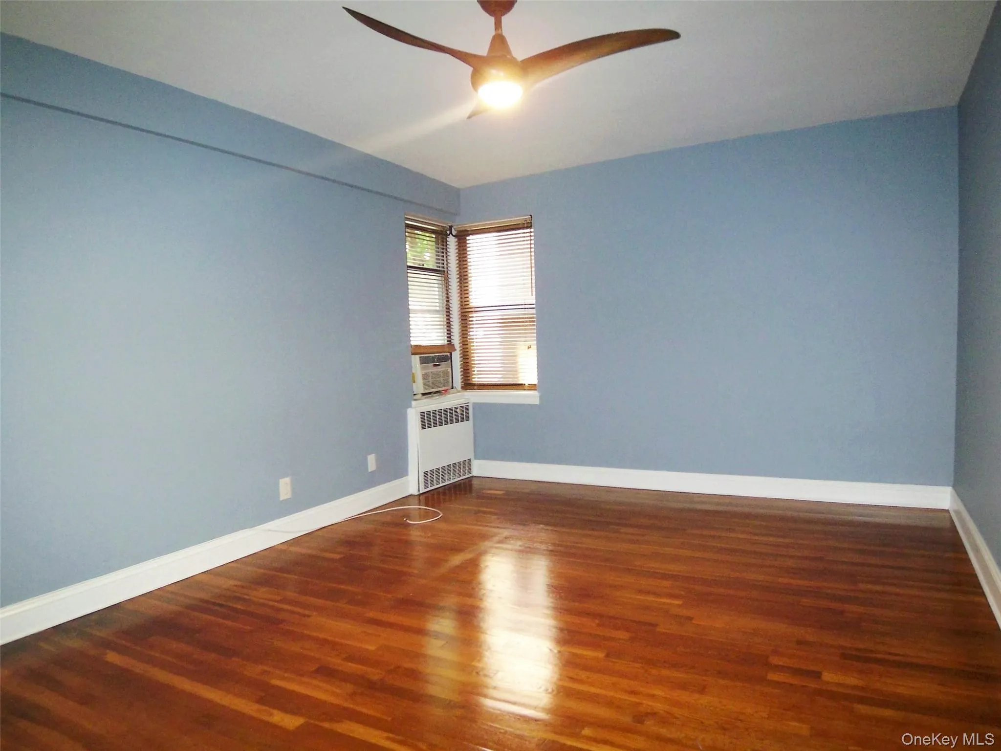 Spare room featuring dark wood finished floors, radiator heating unit, and a ceiling fan Spare room featuring dark wood finished floors, radiator heating unit, and a ceiling fan