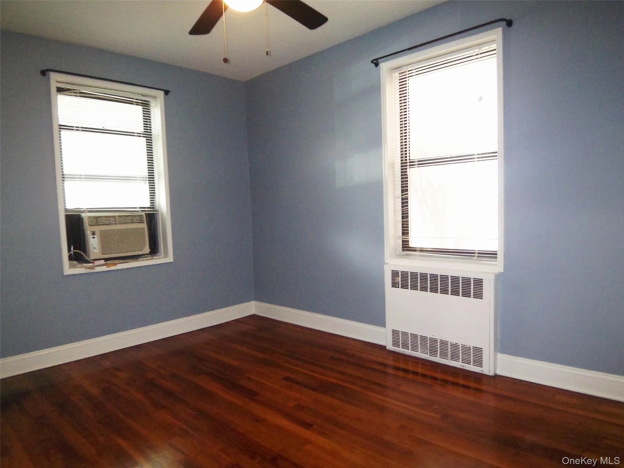 Bedroom featuring radiator, dark wood-style flooring, cooling unit, and a ceiling fan Bedroom featuring radiator, dark wood-style flooring, cooling unit, and a ceiling fan