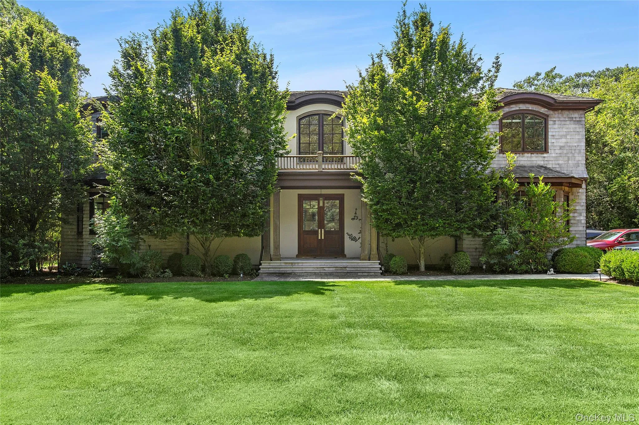 View of front of property with a front lawn, a balcony, french doors, stucco siding, and a porch