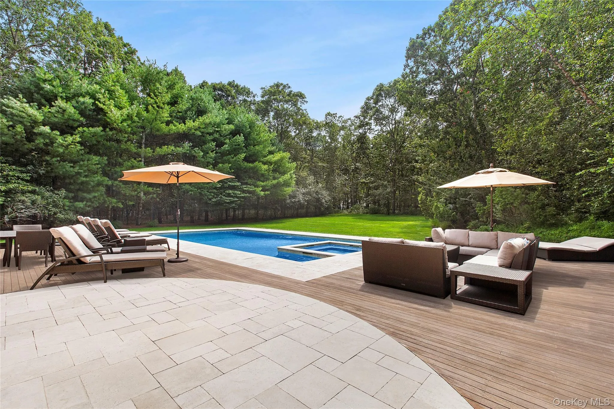 View of pool featuring a deck, an outdoor hangout area, a lawn, a pool with connected hot tub, and a view of trees