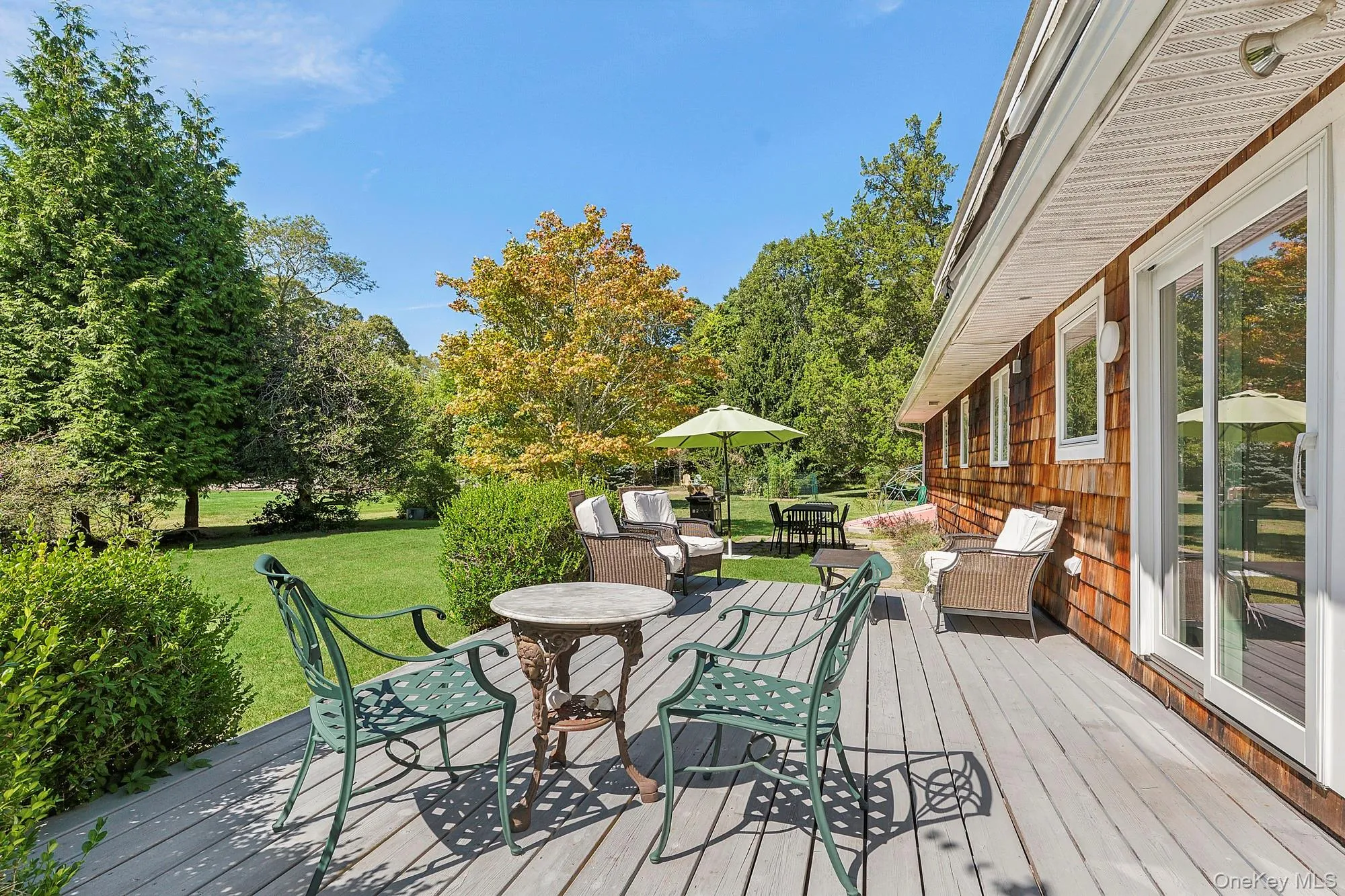 Wooden terrace with outdoor dining area, a lawn, and view of wooded area Wooden terrace with outdoor dining area, a lawn, and view of wooded area