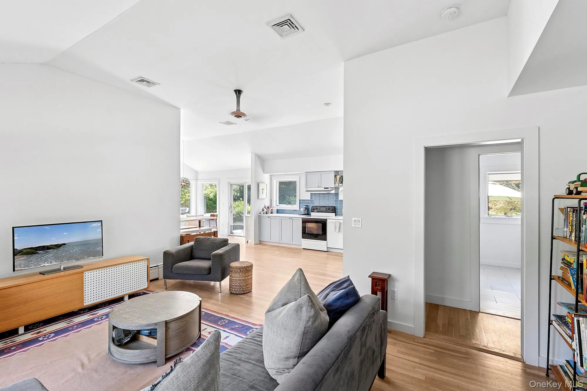 Living room with light wood finished floors, vaulted ceiling, a ceiling fan, and a baseboard radiator Living room with light wood finished floors, vaulted ceiling, a ceiling fan, and a baseboard radiator