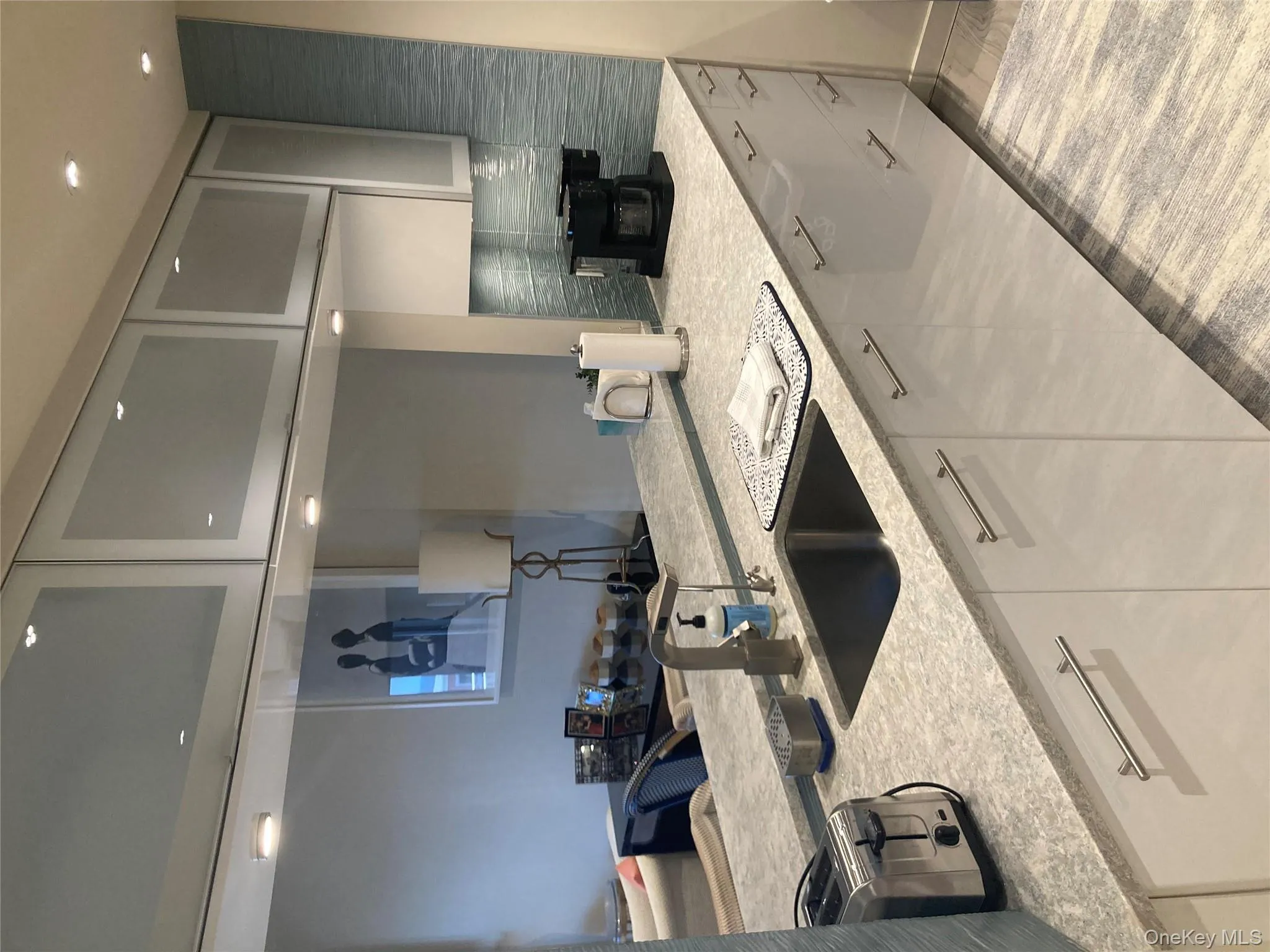 Kitchen with light stone counters, decorative backsplash, glass insert cabinets, light wood-style flooring, and recessed lighting Kitchen with light stone counters, decorative backsplash, glass insert cabinets, light wood-style flooring, and recessed lighting