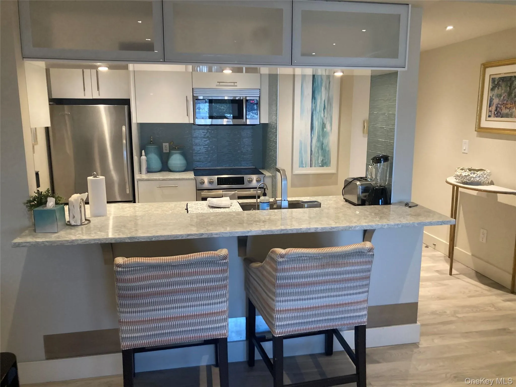 Kitchen with light stone counters, stainless steel appliances, a breakfast bar, light wood-style flooring, and a peninsula Kitchen with light stone counters, stainless steel appliances, a breakfast bar, light wood-style flooring, and a peninsula