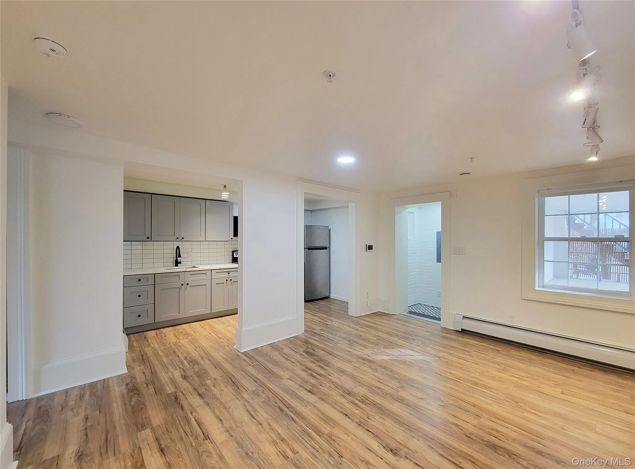 Unfurnished living room with light wood-type flooring, rail lighting, and a baseboard radiator Unfurnished living room with light wood-type flooring, rail lighting, and a baseboard radiator
