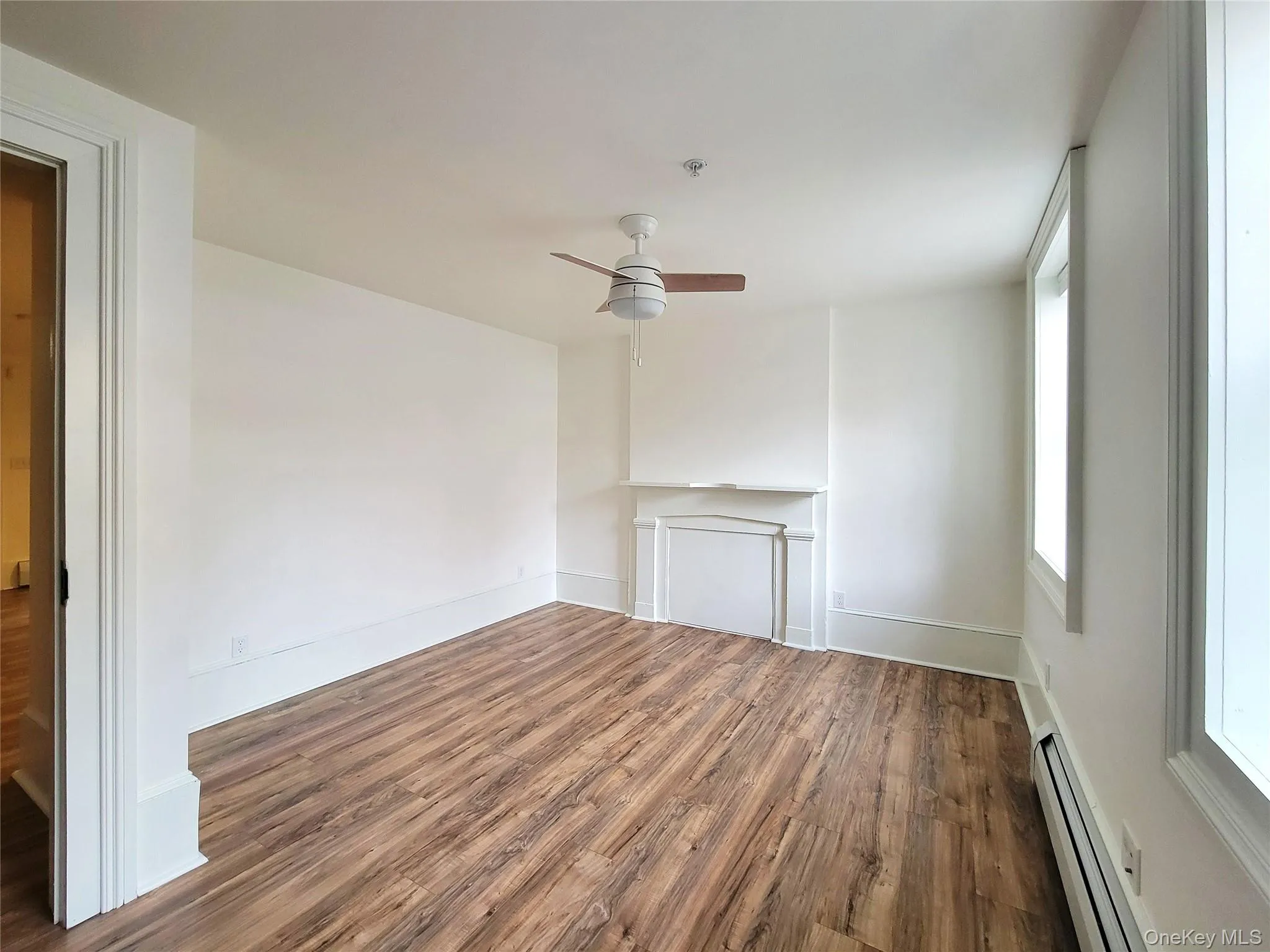 Unfurnished living room featuring wood finished floors, baseboard heating, and a ceiling fan Unfurnished living room featuring wood finished floors, baseboard heating, and a ceiling fan