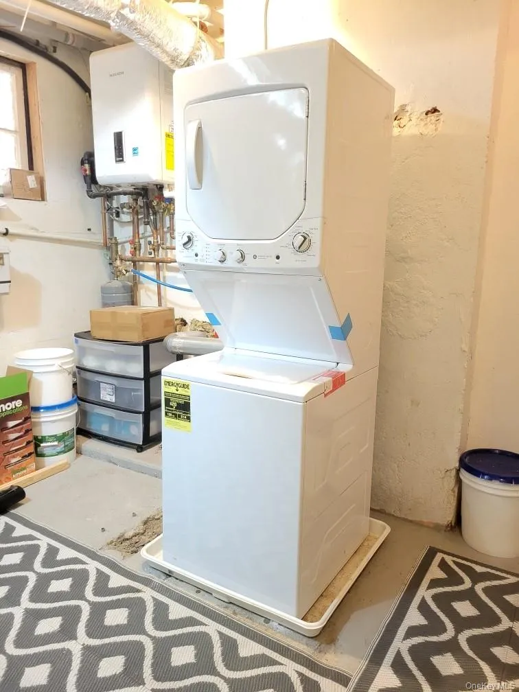 Washroom with stacked washing machine and dryer, tankless water heater, and concrete flooring Washroom with stacked washing machine and dryer, tankless water heater, and concrete flooring