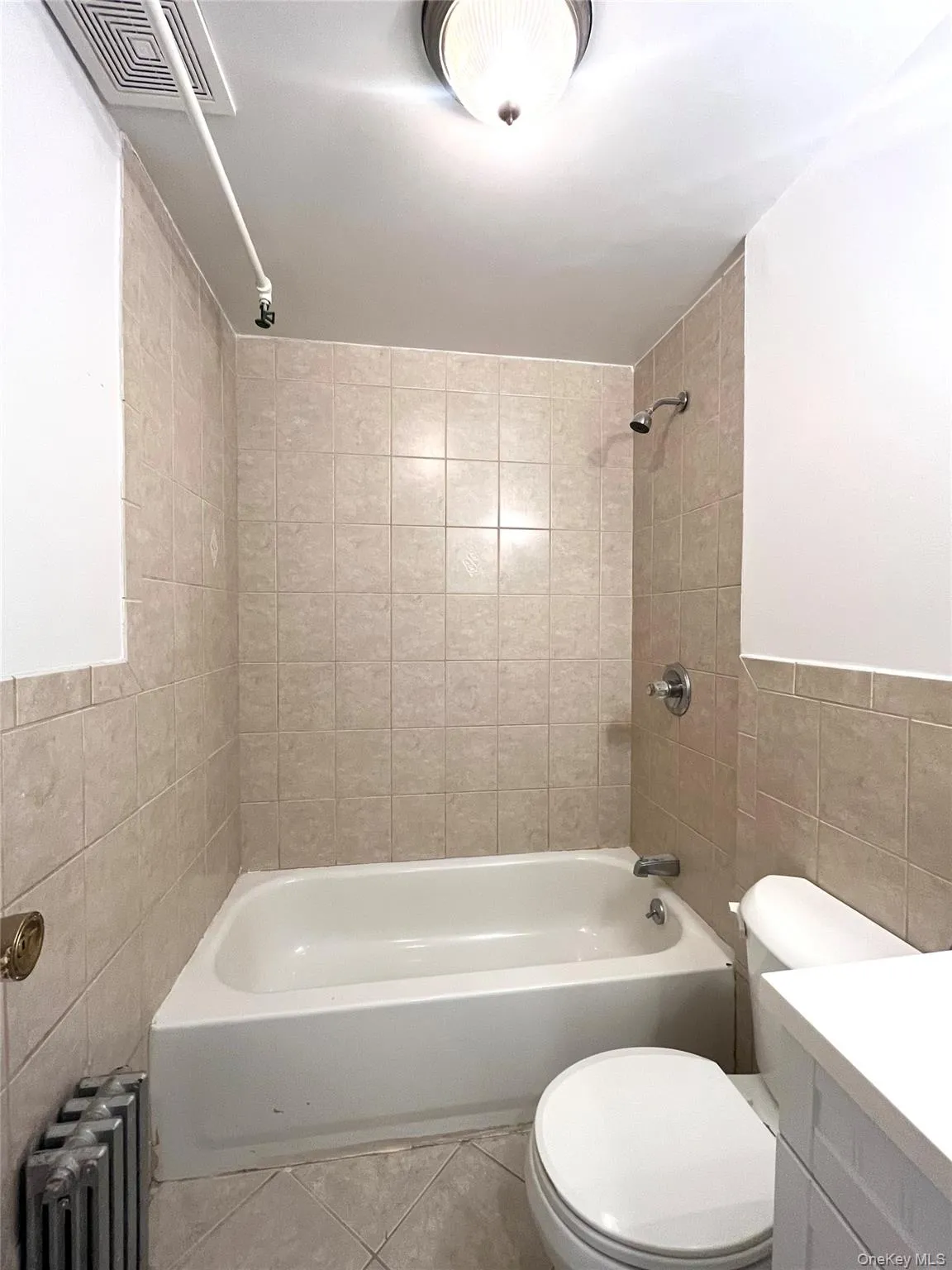 Bathroom featuring tile walls, bathtub / shower combination, radiator heating unit, vanity, and tile patterned floors Bathroom featuring tile walls, bathtub / shower combination, radiator heating unit, vanity, and tile patterned floors