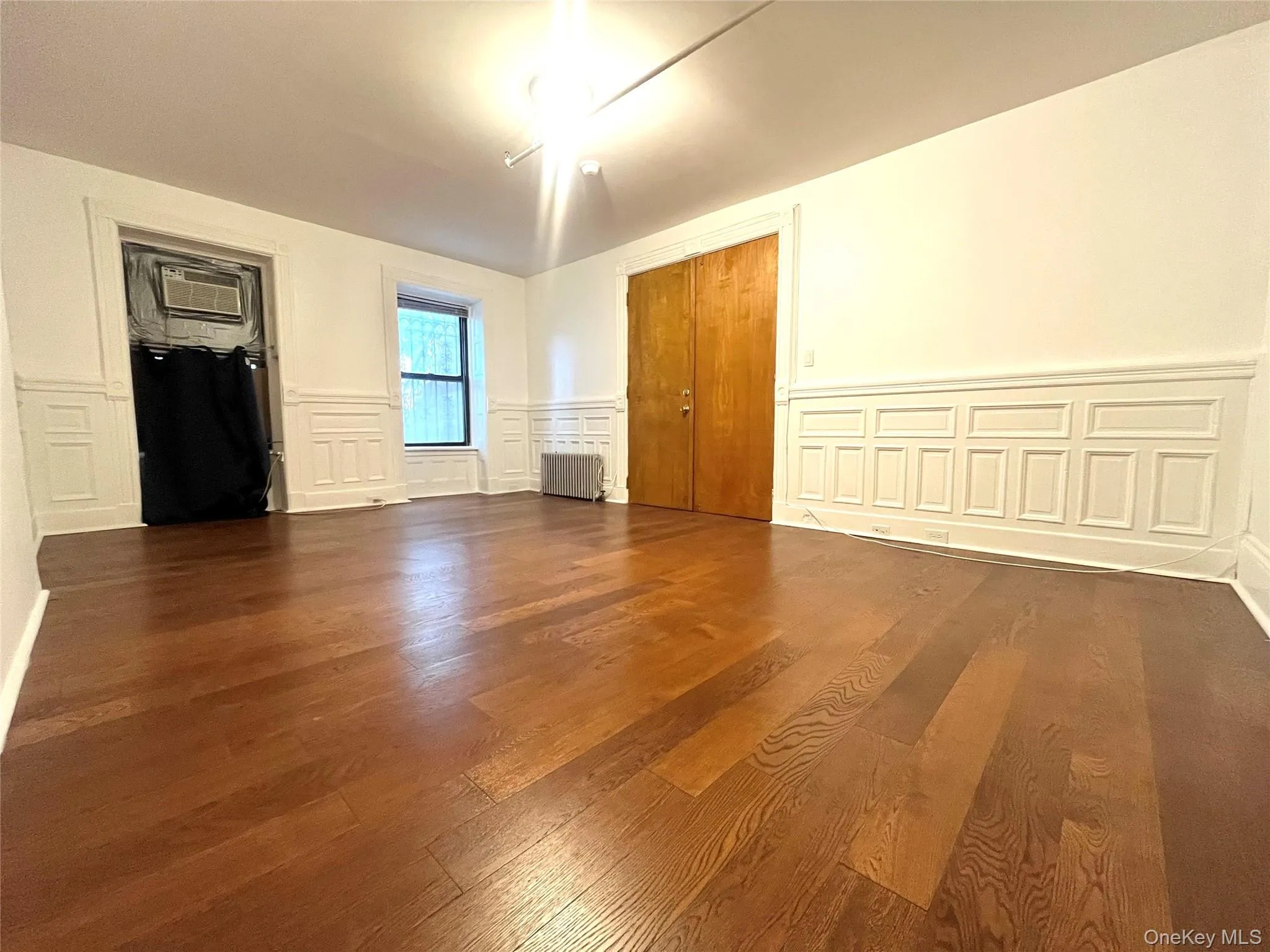 Unfurnished bedroom featuring a decorative wall, wainscoting, dark wood-style flooring, radiator, and a closet Unfurnished bedroom featuring a decorative wall, wainscoting, dark wood-style flooring, radiator, and a closet