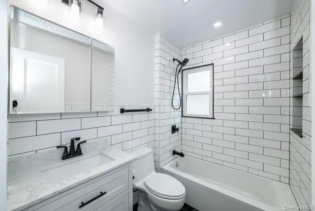 Full bathroom featuring tub / shower combination, vanity, tile walls, tasteful backsplash, and recessed lighting Full bathroom featuring tub / shower combination, vanity, tile walls, tasteful backsplash, and recessed lighting