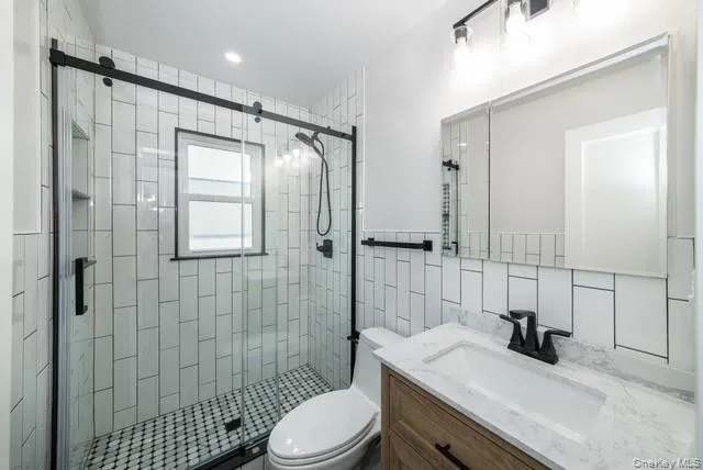 Bathroom featuring vanity, a stall shower, and tile walls Bathroom featuring vanity, a stall shower, and tile walls