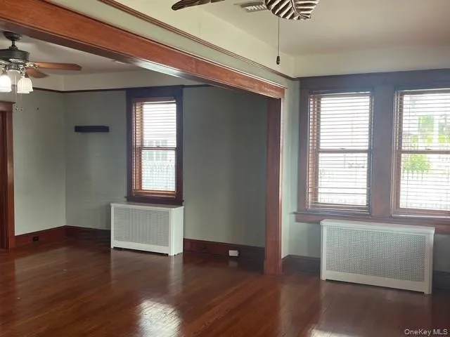 Unfurnished room with radiator heating unit, a ceiling fan, and dark wood-style floors Unfurnished room with radiator heating unit, a ceiling fan, and dark wood-style floors