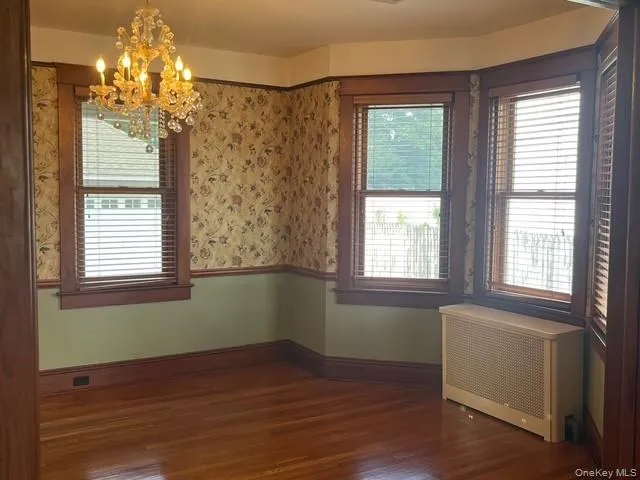 Spare room featuring radiator heating unit, a chandelier, and dark wood-type flooring Spare room featuring radiator heating unit, a chandelier, and dark wood-type flooring