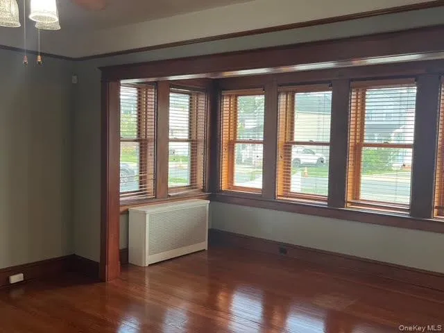 Empty room featuring dark wood-style floors, radiator heating unit, and ceiling fan Empty room featuring dark wood-style floors, radiator heating unit, and ceiling fan