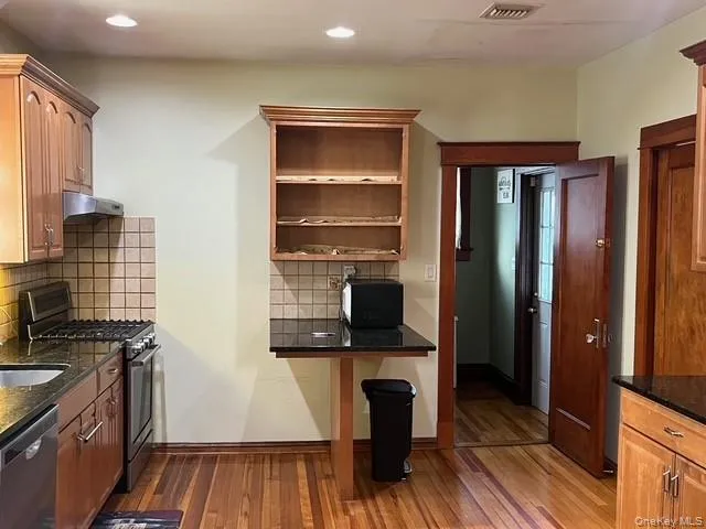 Kitchen with appliances with stainless steel finishes, open shelves, dark stone counters, brown cabinets, and recessed lighting Kitchen with appliances with stainless steel finishes, open shelves, dark stone counters, brown cabinets, and recessed lighting