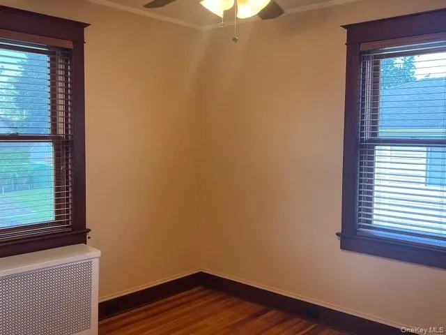 Unfurnished room featuring radiator heating unit, dark wood-style floors, ornamental molding, and ceiling fan Unfurnished room featuring radiator heating unit, dark wood-style floors, ornamental molding, and ceiling fan