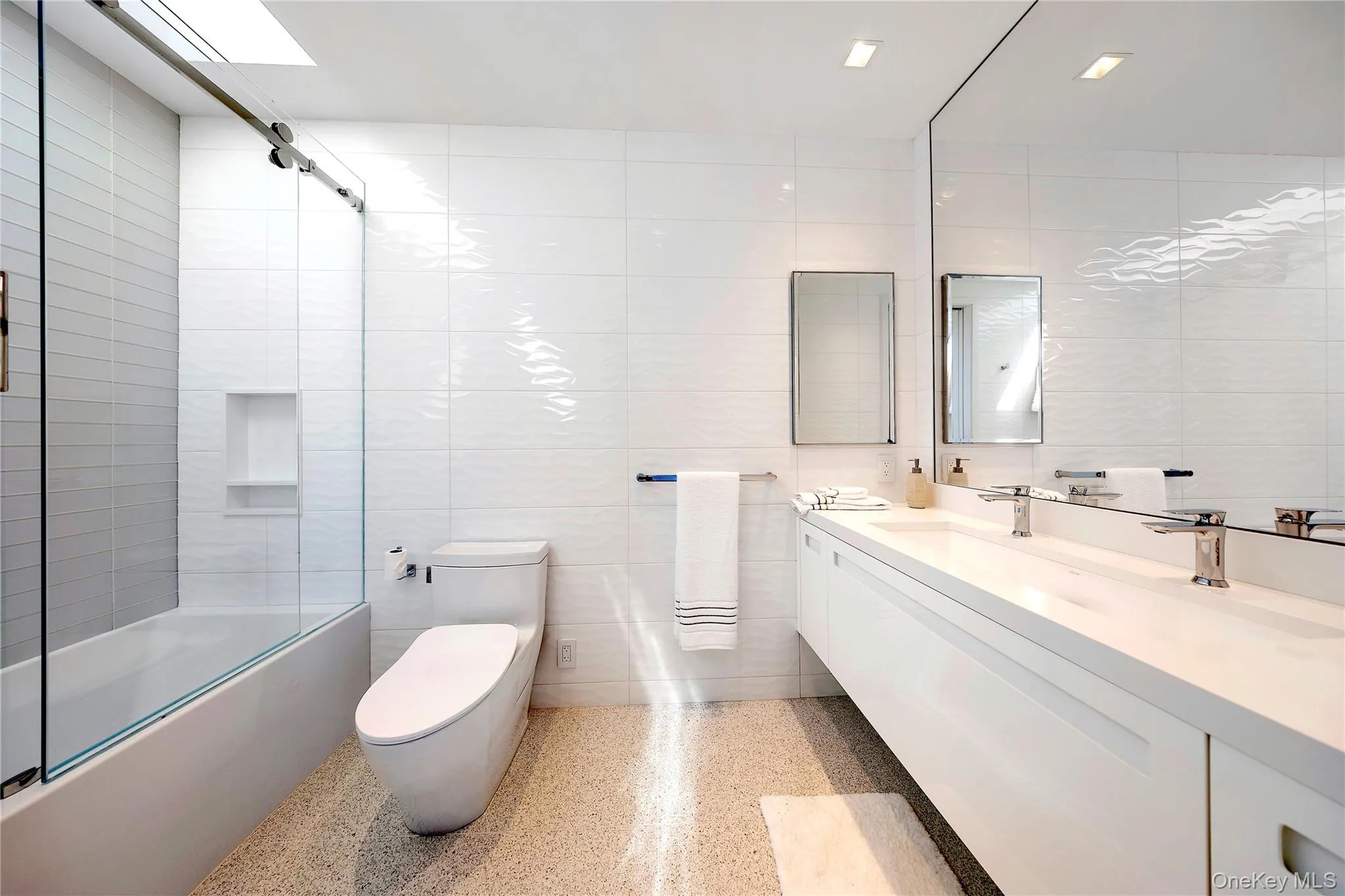 Bathroom featuring tile walls, combined bath / shower with glass door, vanity, and dark speckled floor Bathroom featuring tile walls, combined bath / shower with glass door, vanity, and dark speckled floor