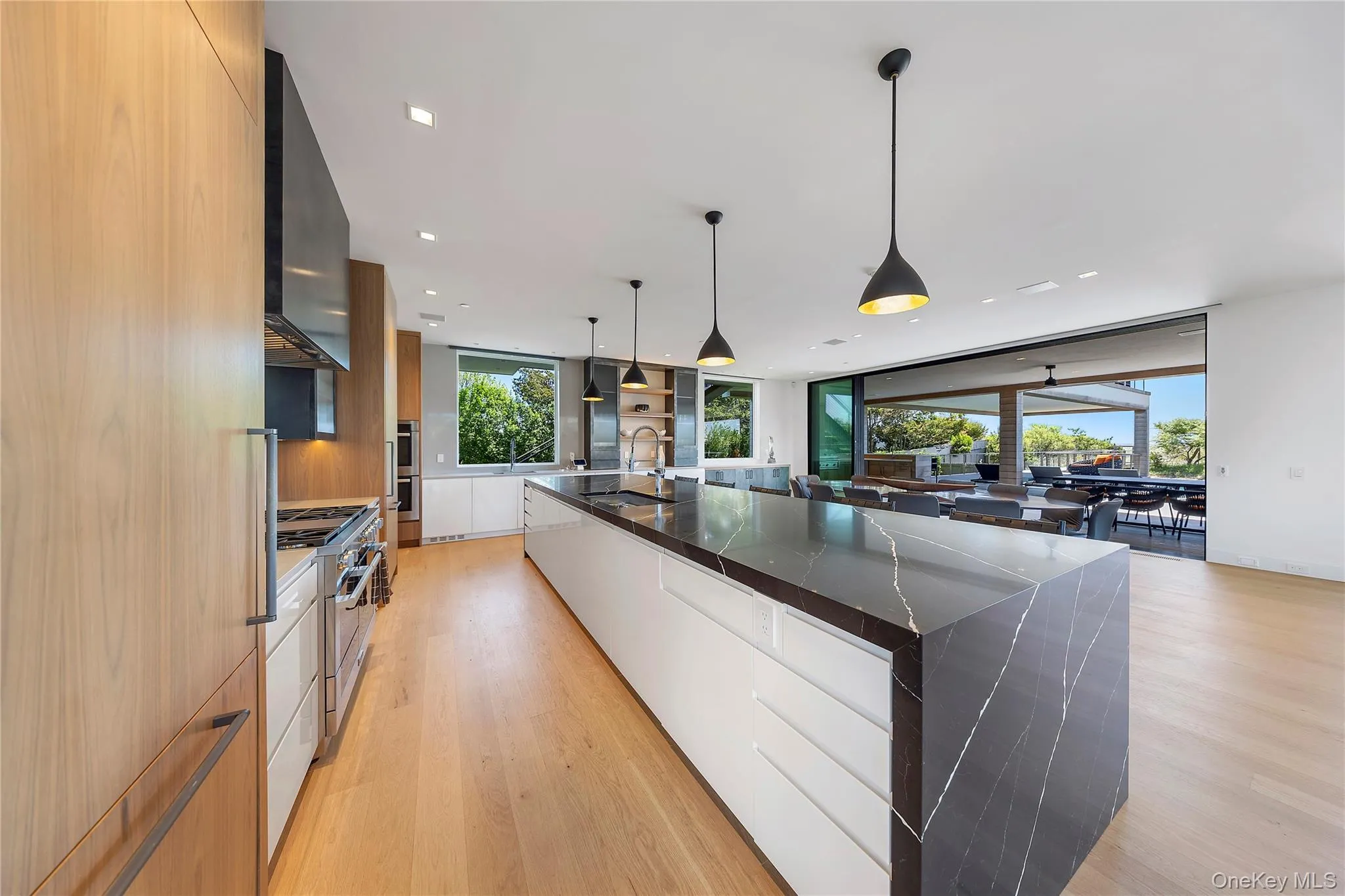 Kitchen with modern cabinets, light wood-style floors, dark stone countertops, decorative light fixtures, and floor to ceiling windows Kitchen with modern cabinets, light wood-style floors, dark stone countertops, decorative light fixtures, and floor to ceiling windows