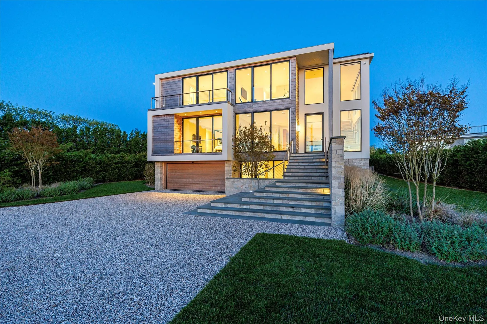 Back of house with stairs, driveway, an attached garage, a balcony, and stone siding Back of house with stairs, driveway, an attached garage, a balcony, and stone siding