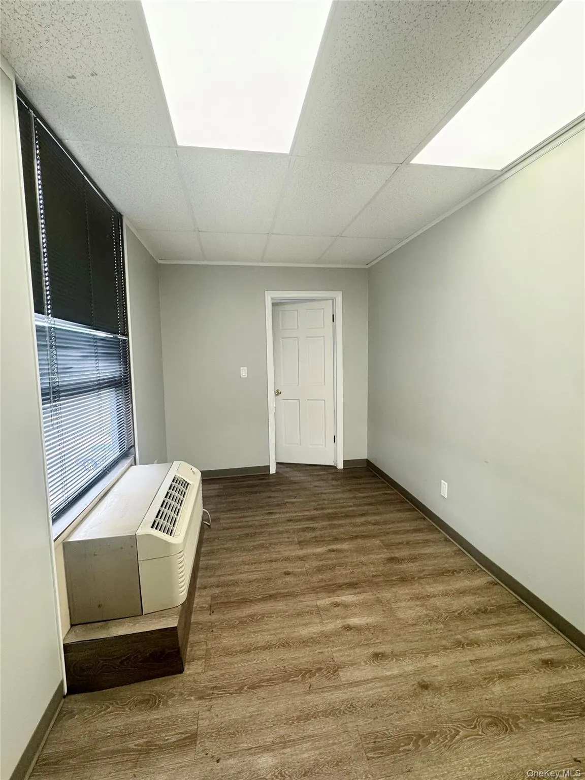 Empty room with wood finished floors, a wall mounted AC, and a paneled ceiling Empty room with wood finished floors, a wall mounted AC, and a paneled ceiling