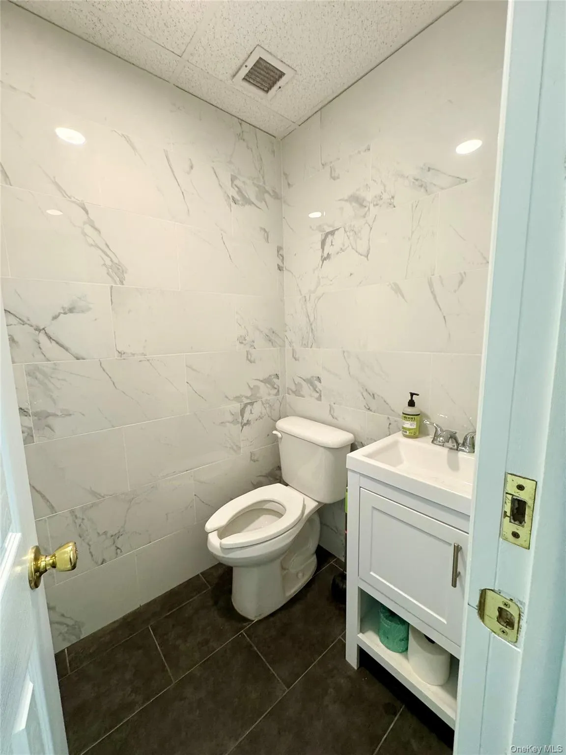 Bathroom featuring tile walls, vanity, and dark tile patterned floors Bathroom featuring tile walls, vanity, and dark tile patterned floors