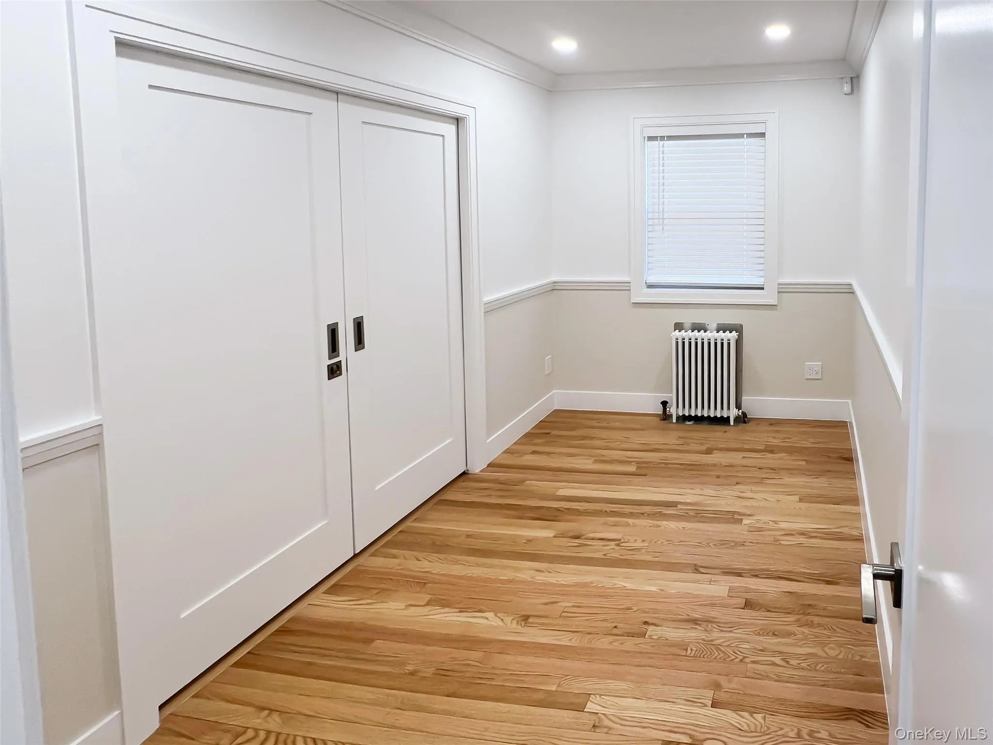Unfurnished bedroom featuring radiator, light wood-style flooring, ornamental molding, a closet, and recessed lighting Unfurnished bedroom featuring radiator, light wood-style flooring, ornamental molding, a closet, and recessed lighting