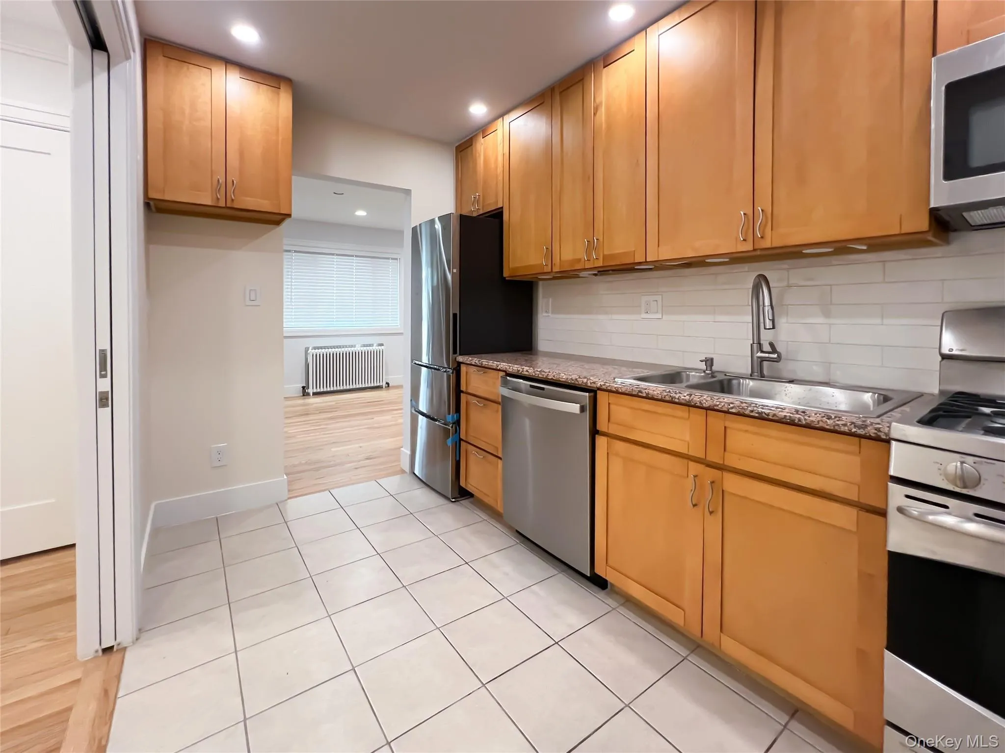 Kitchen featuring appliances with stainless steel finishes, light tile patterned flooring, backsplash, radiator, and recessed lighting Kitchen featuring appliances with stainless steel finishes, light tile patterned flooring, backsplash, radiator, and recessed lighting