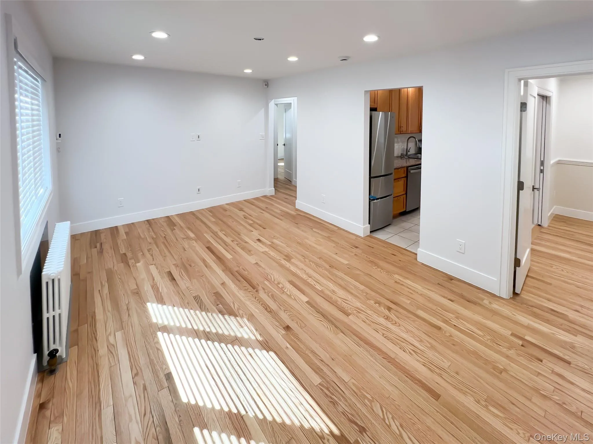Unfurnished bedroom with recessed lighting, light wood-type flooring, radiator, and freestanding refrigerator Unfurnished bedroom with recessed lighting, light wood-type flooring, radiator, and freestanding refrigerator