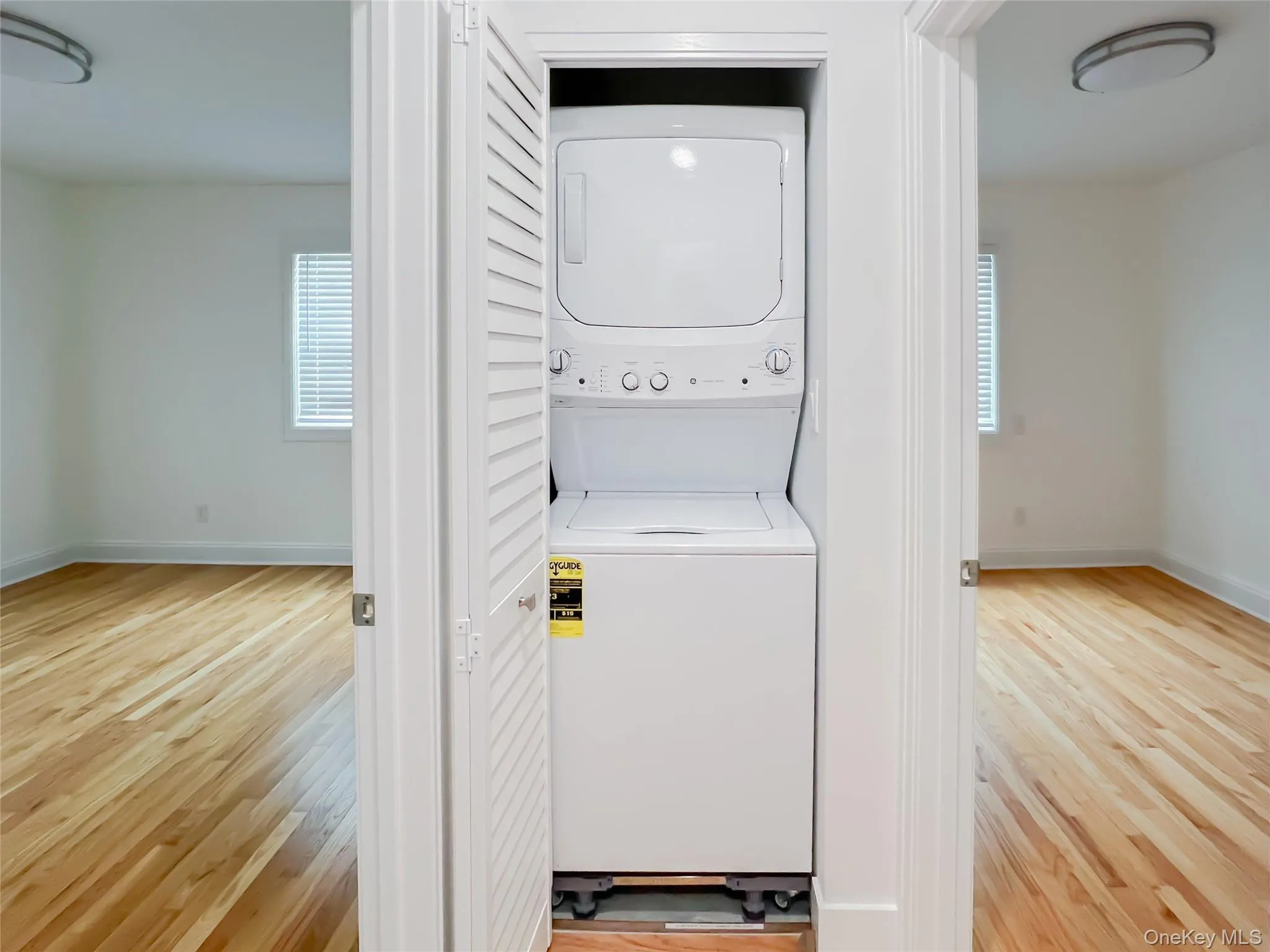 Washroom with light wood-style flooring and stacked washing machine and dryer Washroom with light wood-style flooring and stacked washing machine and dryer