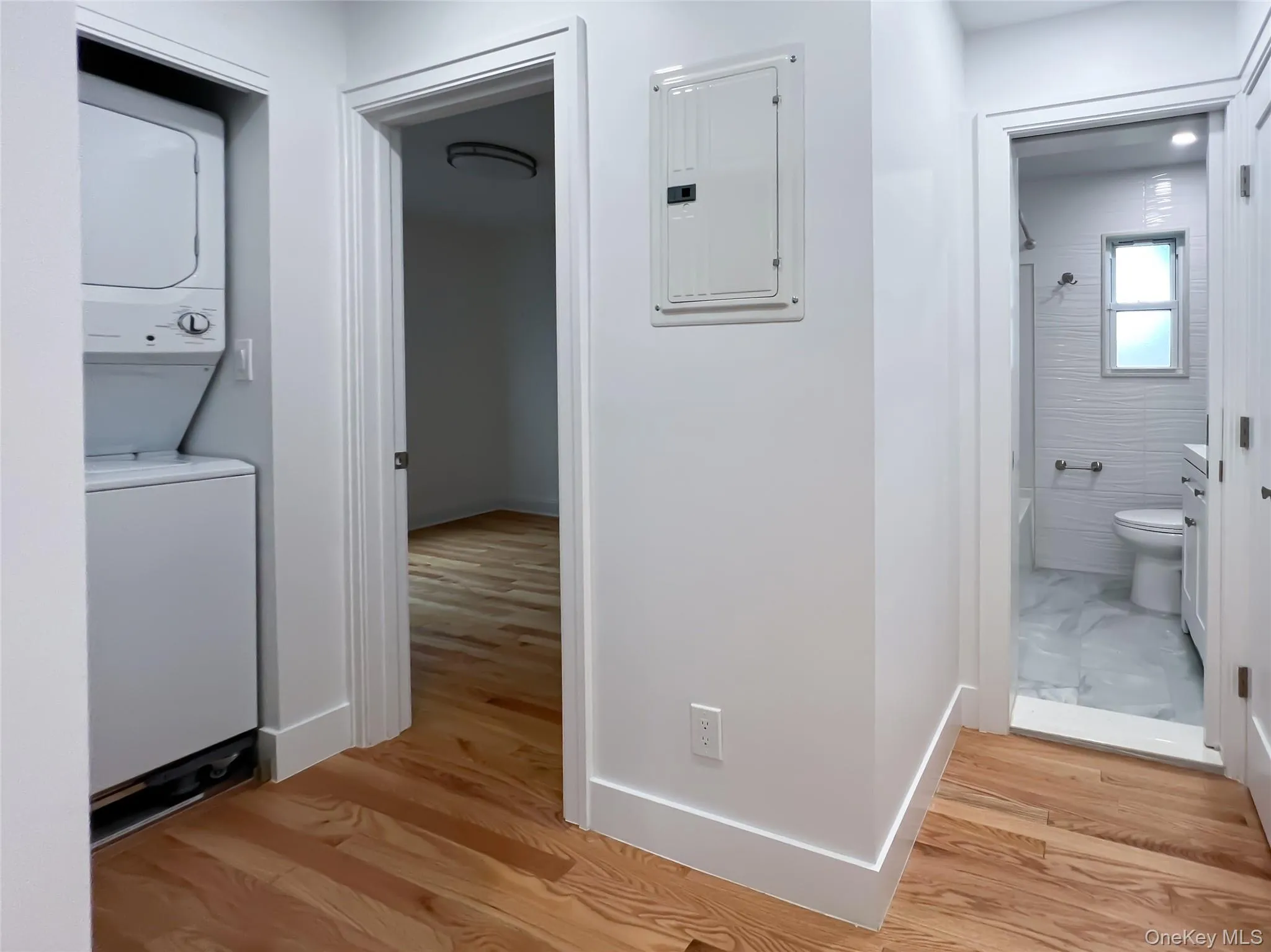 Hall with electric panel, estacked washer and dryer, and light wood-style floors Hall with electric panel, estacked washer and dryer, and light wood-style floors