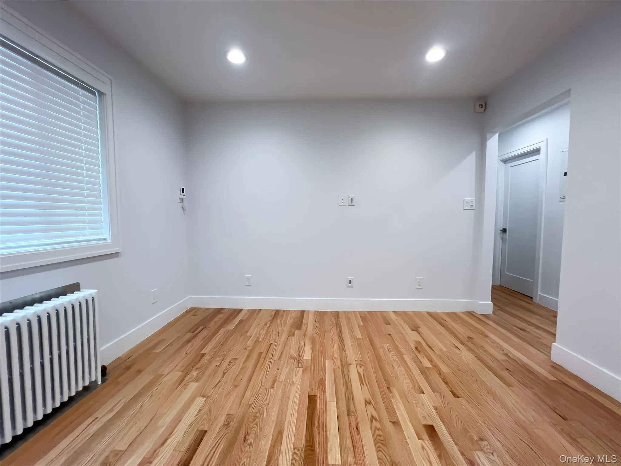 Empty room featuring radiator heating unit, light wood-style floors, and recessed lighting Empty room featuring radiator heating unit, light wood-style floors, and recessed lighting