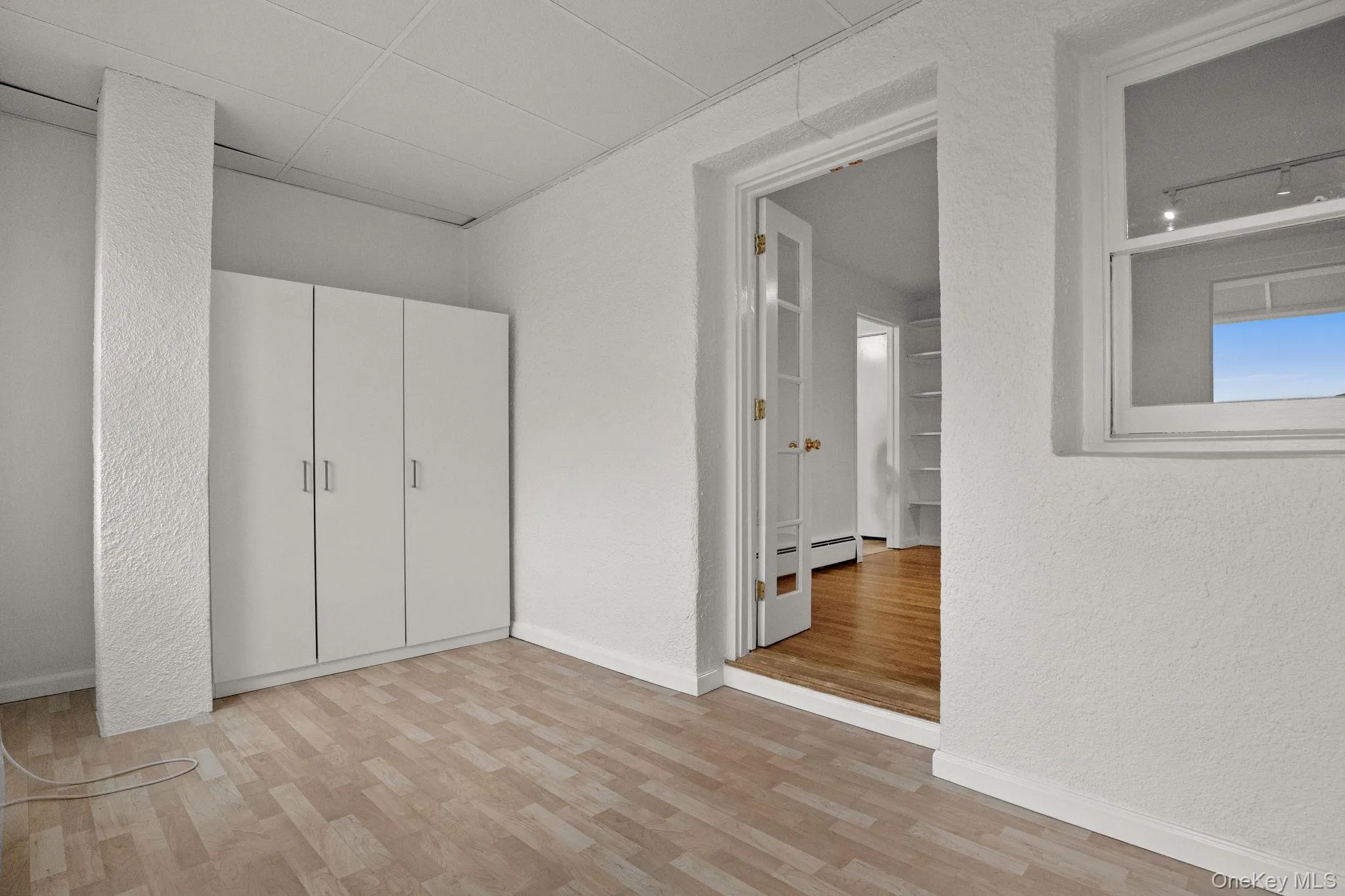 Unfurnished bedroom featuring a textured wall, light wood-type flooring, and a drop ceiling Unfurnished bedroom featuring a textured wall, light wood-type flooring, and a drop ceiling