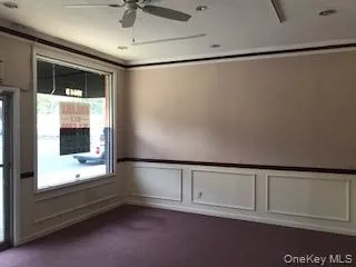 Unfurnished room featuring dark carpet, a wainscoted wall, a decorative wall, a ceiling fan, and crown molding Unfurnished room featuring dark carpet, a wainscoted wall, a decorative wall, a ceiling fan, and crown molding