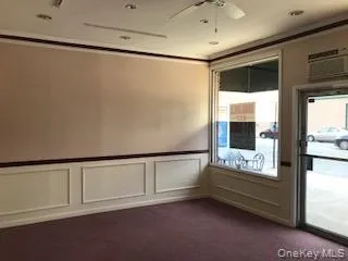 Empty room featuring a decorative wall, dark carpet, a wainscoted wall, a ceiling fan, and an AC wall unit Empty room featuring a decorative wall, dark carpet, a wainscoted wall, a ceiling fan, and an AC wall unit