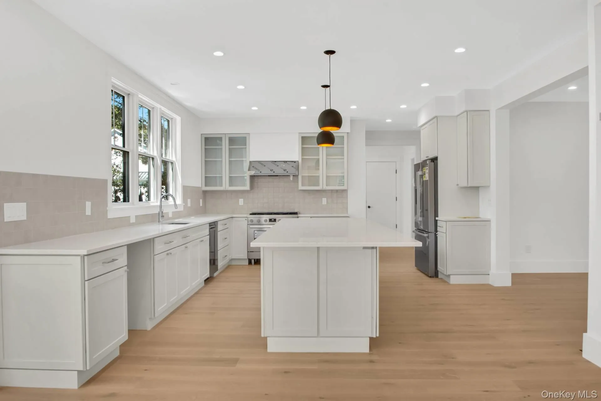 Kitchen featuring a kitchen island, glass insert cabinets, white cabinets, light wood-style flooring, and decorative backsplash Kitchen featuring a kitchen island, glass insert cabinets, white cabinets, light wood-style flooring, and decorative backsplash