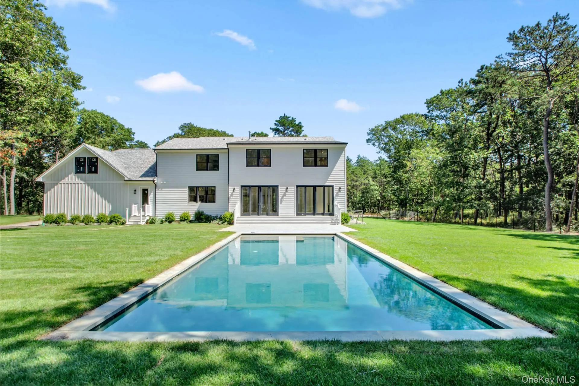 Rear view of property with a lawn, a patio, an outdoor pool, and board and batten siding Rear view of property with a lawn, a patio, an outdoor pool, and board and batten siding
