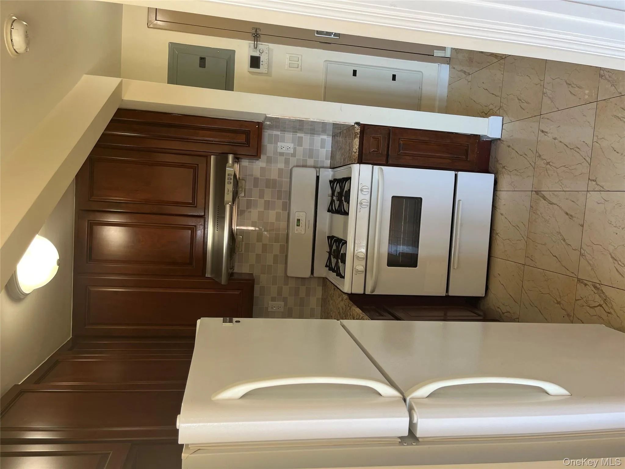 Kitchen with refrigerator, gas range gas stove, backsplash, dark brown cabinetry, and light marble finish flooring Kitchen with refrigerator, gas range gas stove, backsplash, dark brown cabinetry, and light marble finish flooring